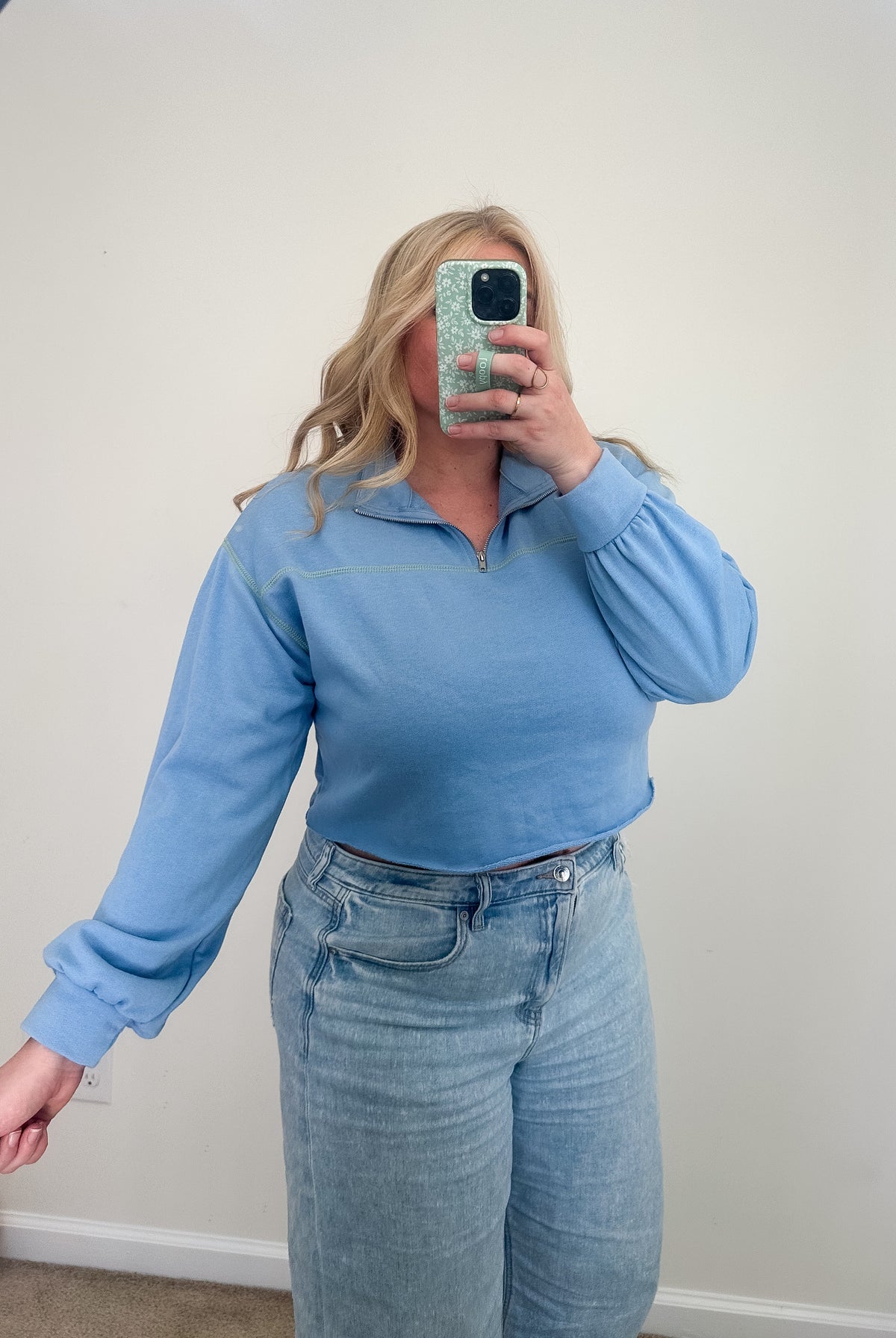 Person wearing a blue long-sleeve top and jeans taking a mirror selfie.
