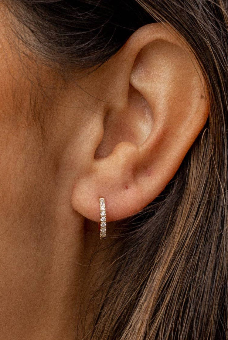 Close-up of an ear wearing a diamond hoop earring with hair partially covering the frame.