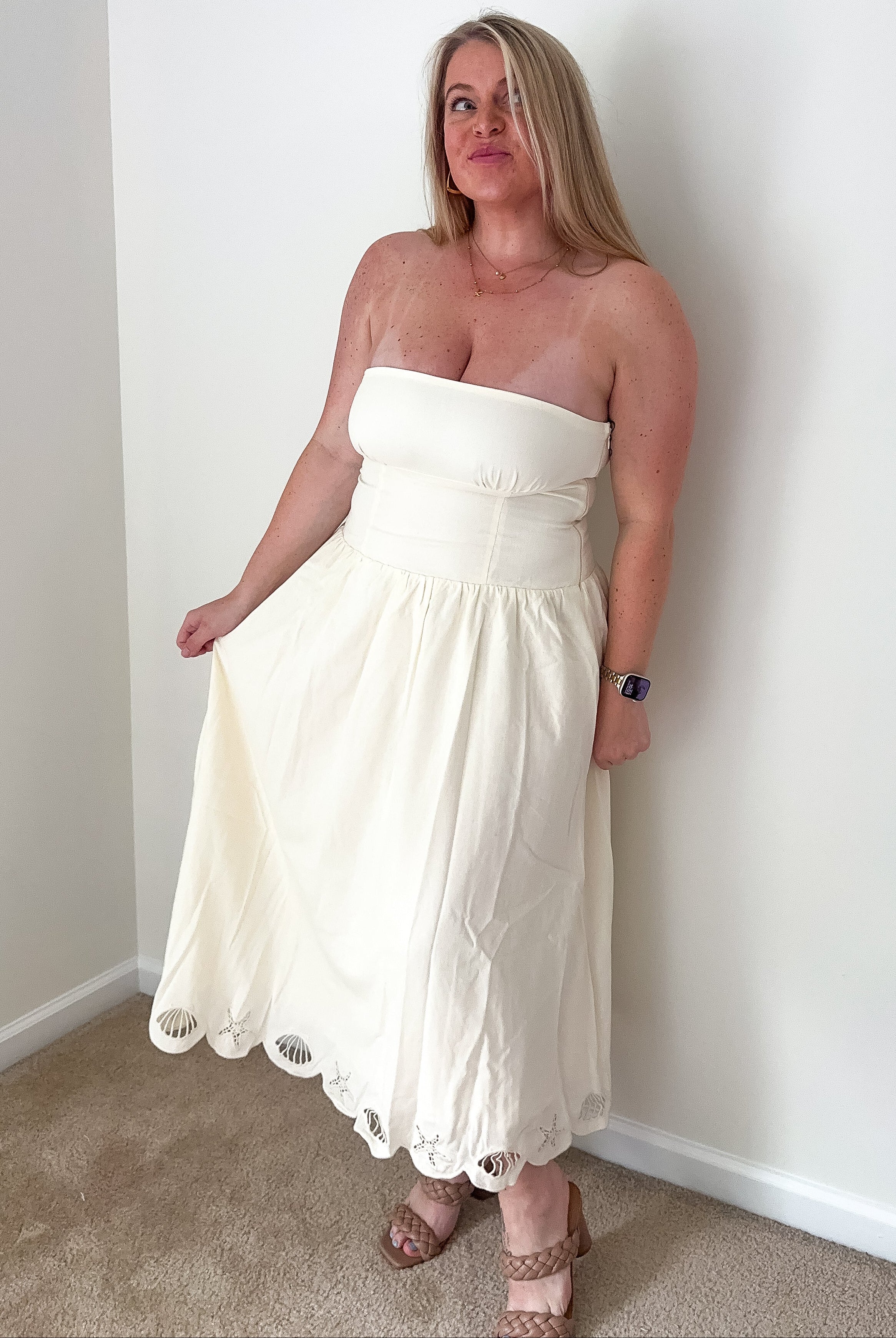 Woman wearing a white strapless dress standing against a plain wall.
