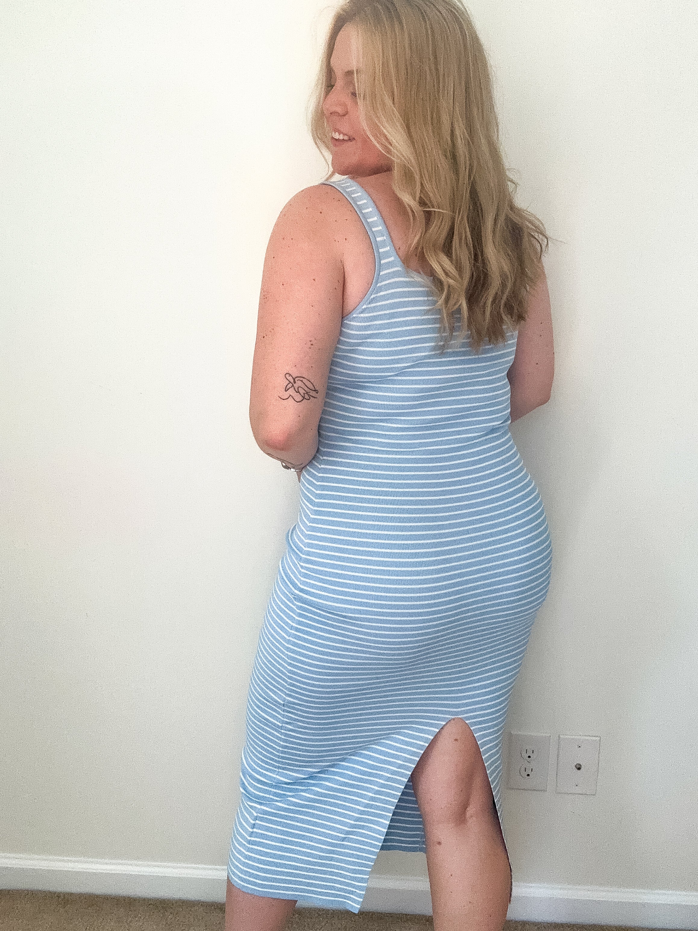 Woman wearing a blue and white striped dress against a plain wall.