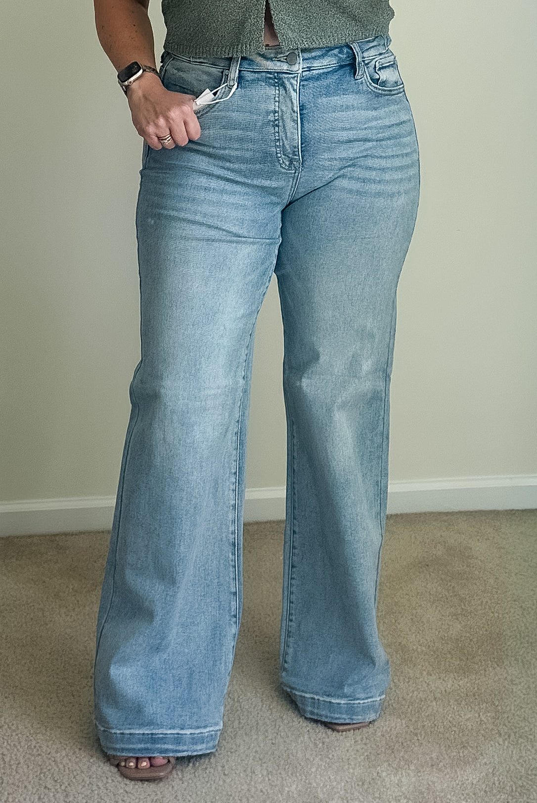 High-rise wide-leg jeans in light wash denim with a button and zip fly, shown worn on a person standing on carpet.
