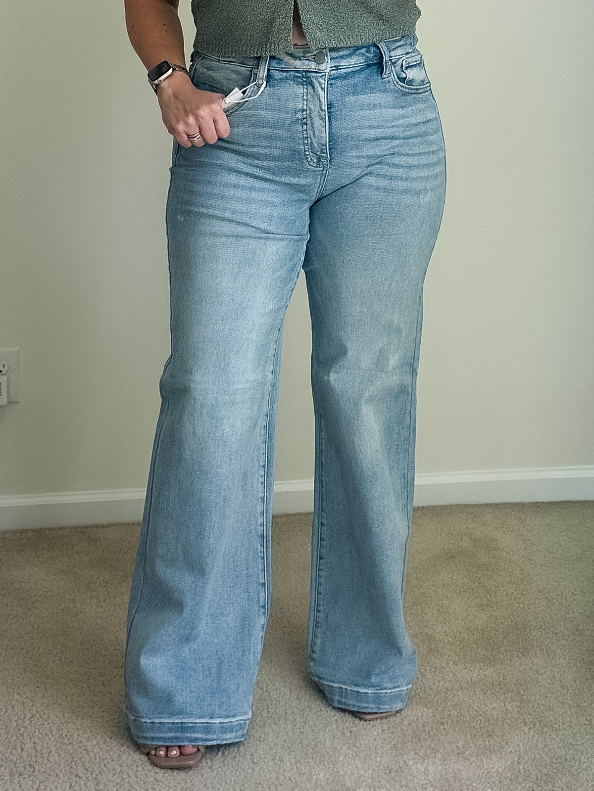 High-rise wide-leg jeans in light wash denim with a button and zip fly, shown worn on a person standing on carpet.