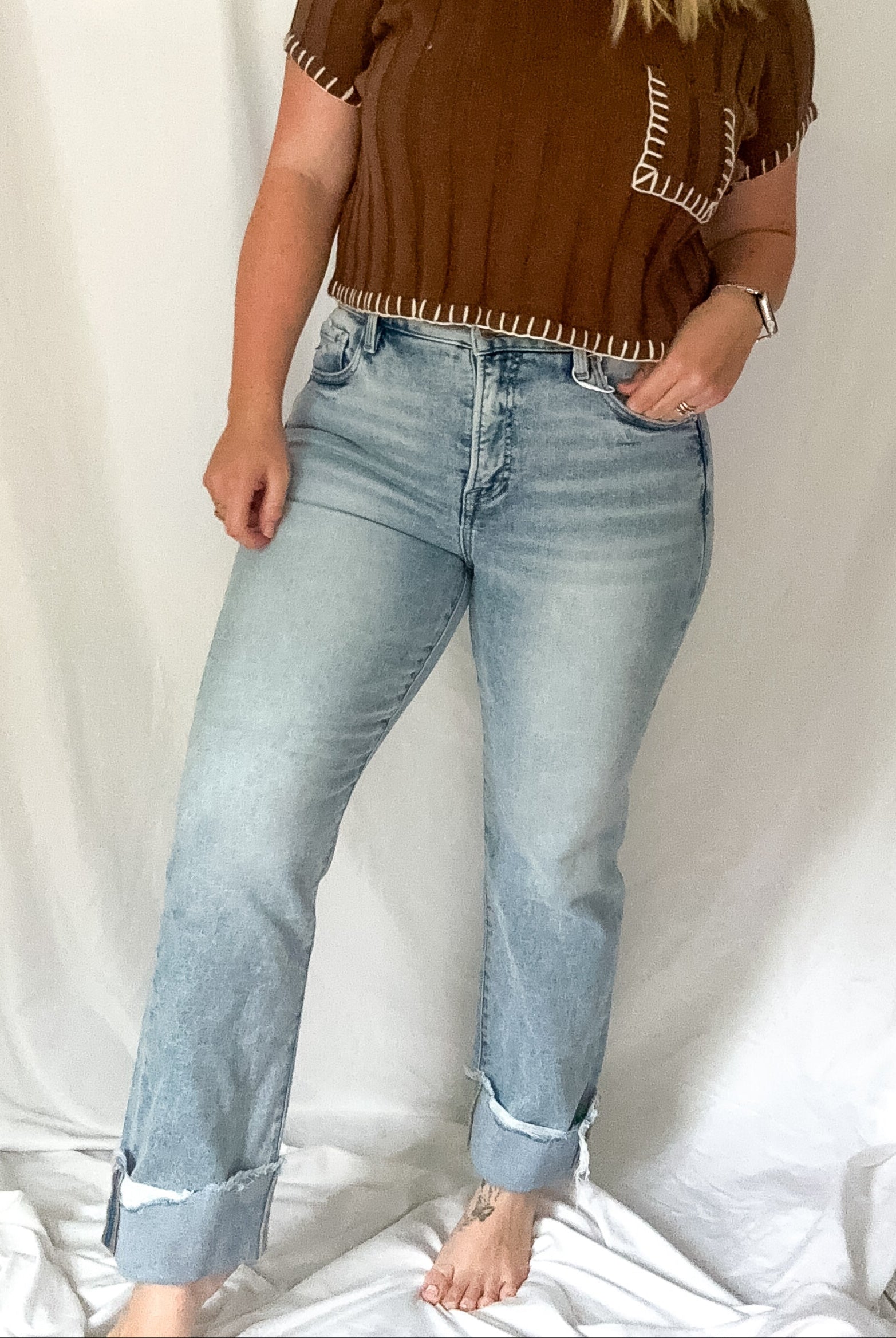 Woman wearing a brown top and light blue jeans against a white background