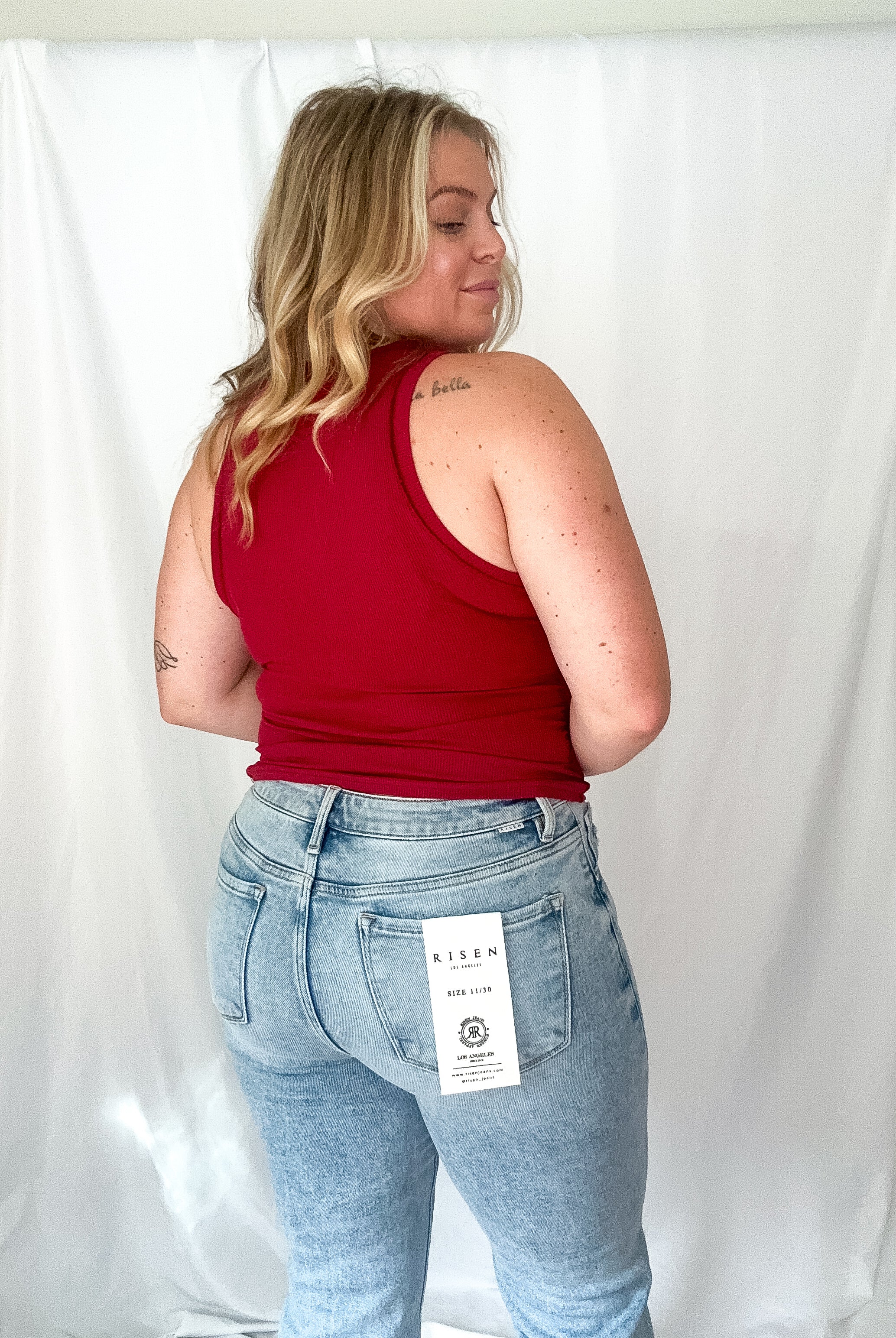 Person wearing a red tank top and light blue jeans with a visible brand tag against a white background