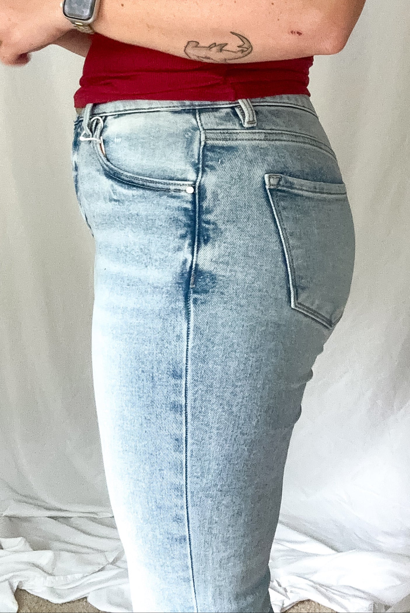 Person wearing a red tank top and light blue jeans against a plain background