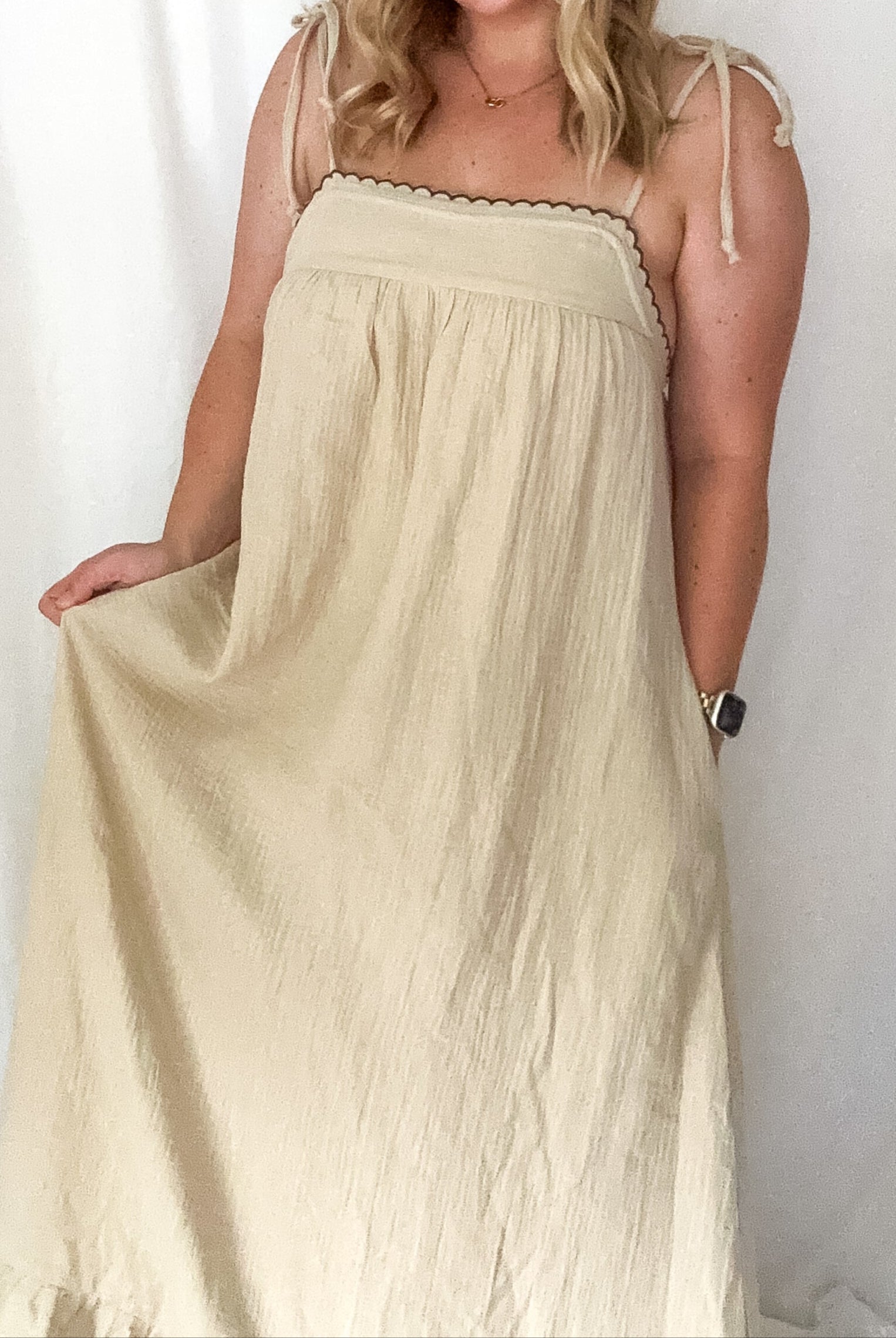 A beige maxi dress with adjustable tie straps and delicate embroidered details, worn by a person.