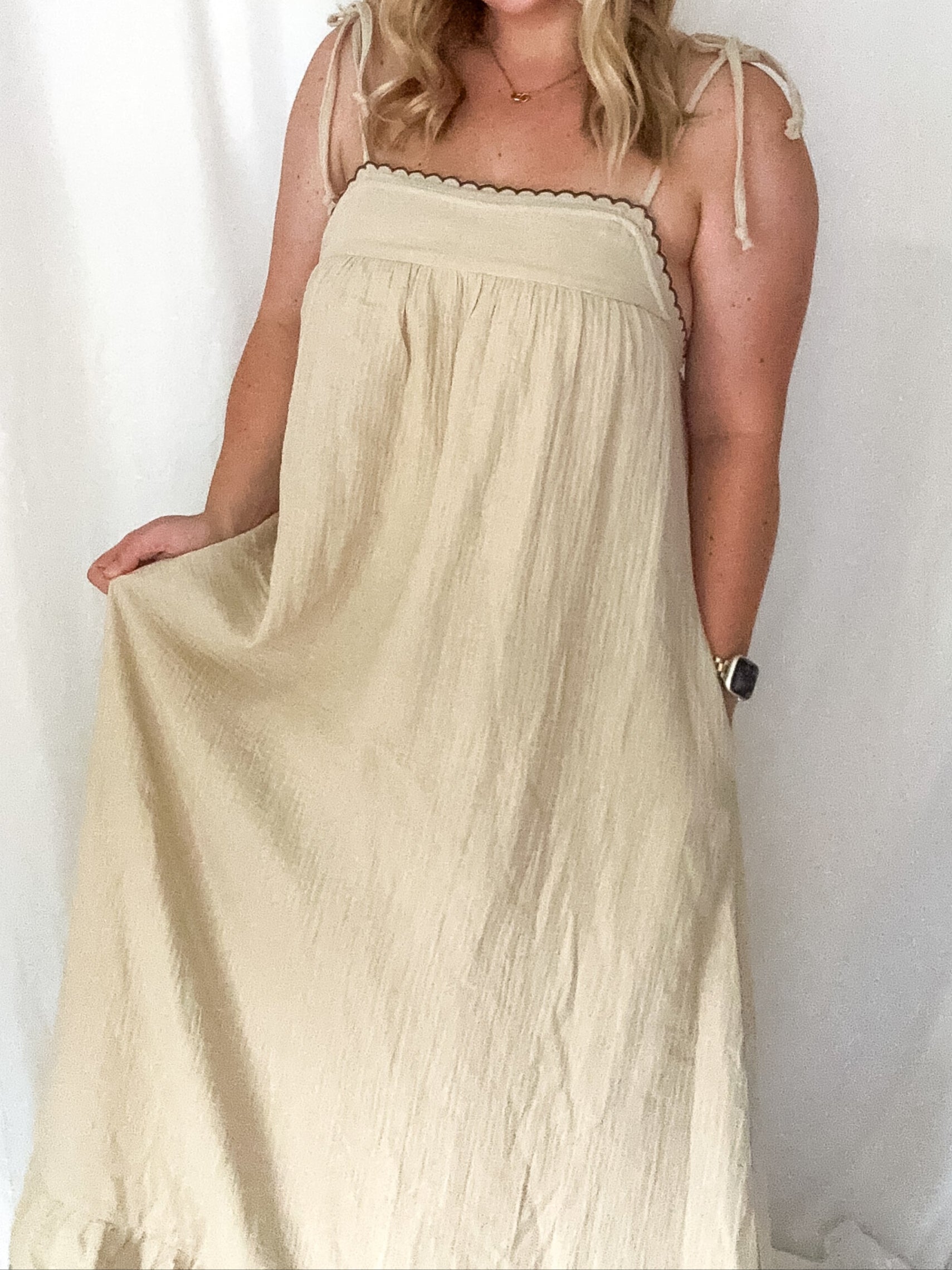 A beige maxi dress with adjustable tie straps and delicate embroidered details, worn by a person.