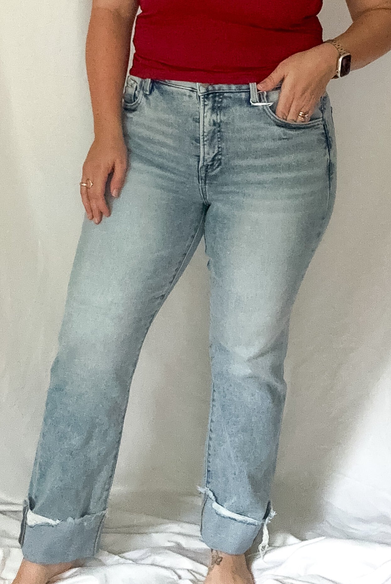 Woman wearing a red top and light blue jeans against a white curtain background