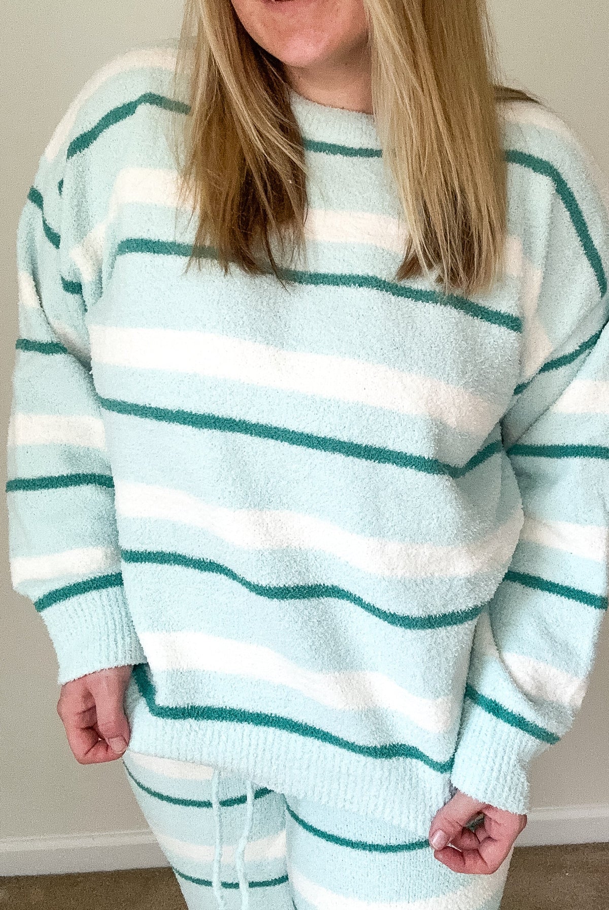 Person wearing a light blue and white striped sweater and pants indoors.