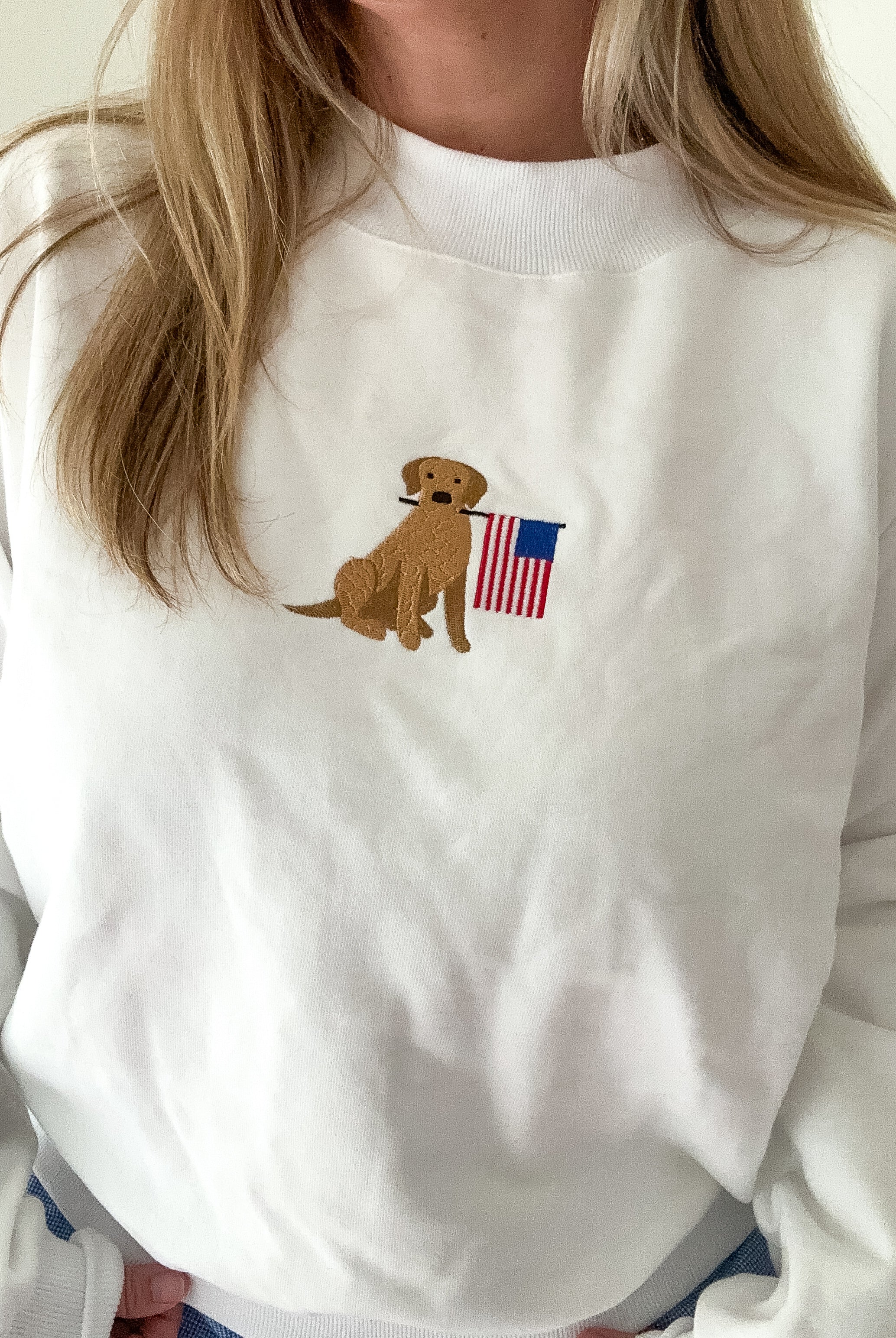 White sweatshirt with a dog holding an American flag patch worn by a person.