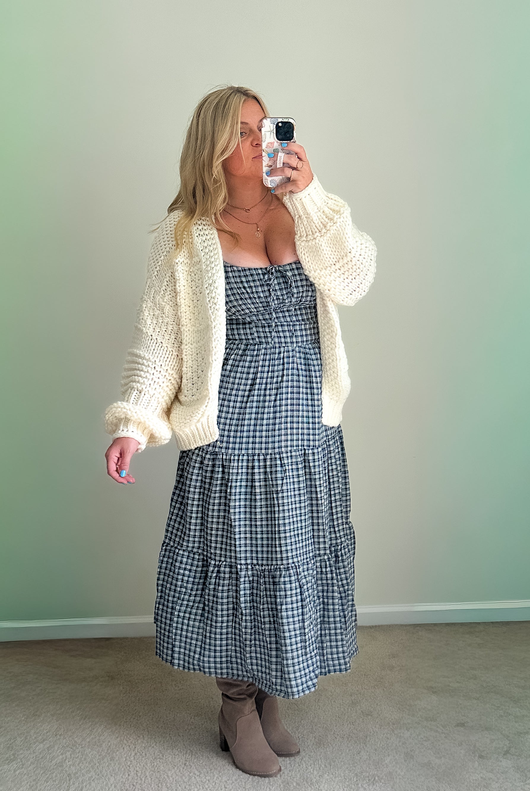 A woman wearing a cream-colored oversized sweater cardigan over a checkered dress.