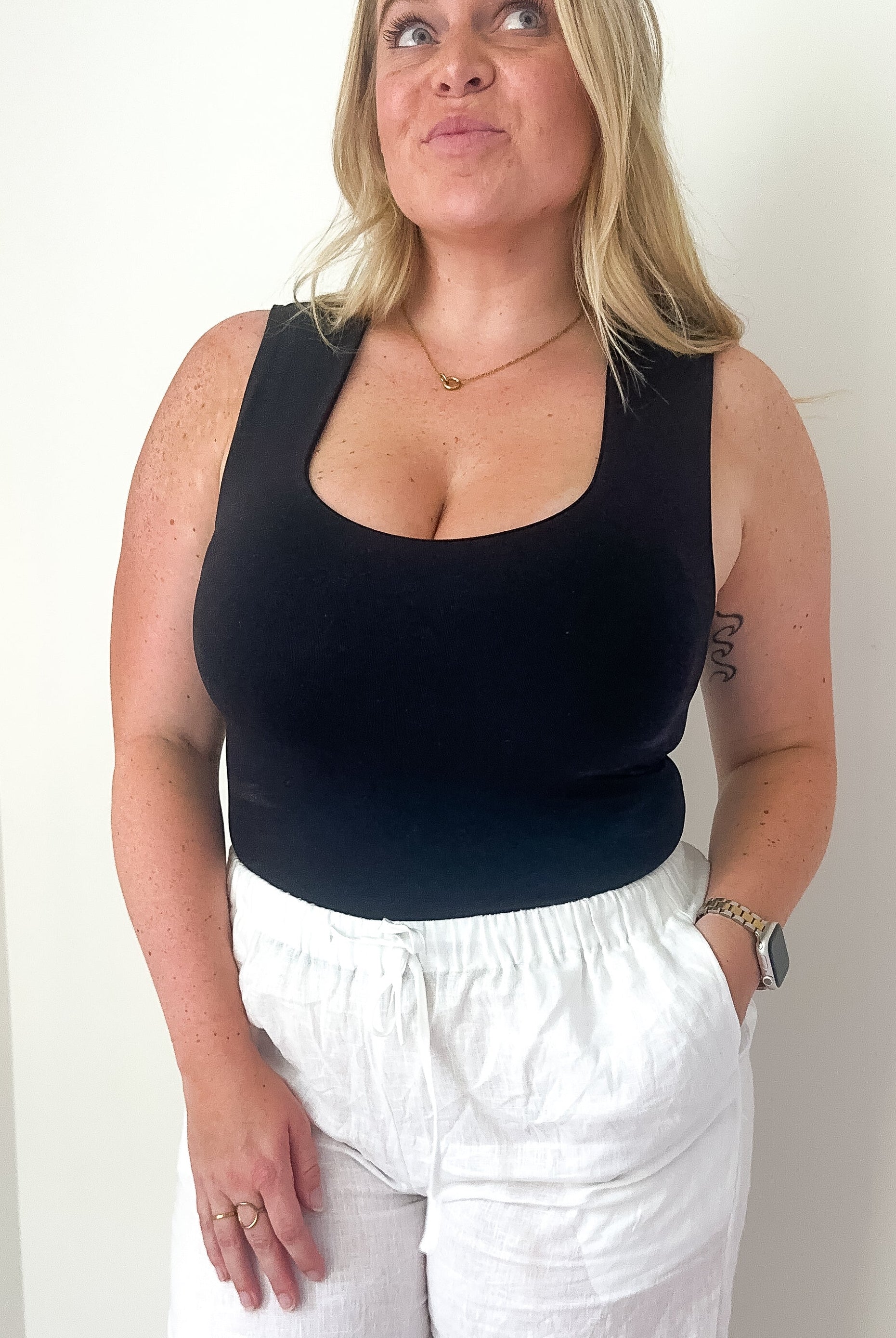 A woman wearing a black sleeveless crop tank with white pants, showcasing a fitted silhouette.