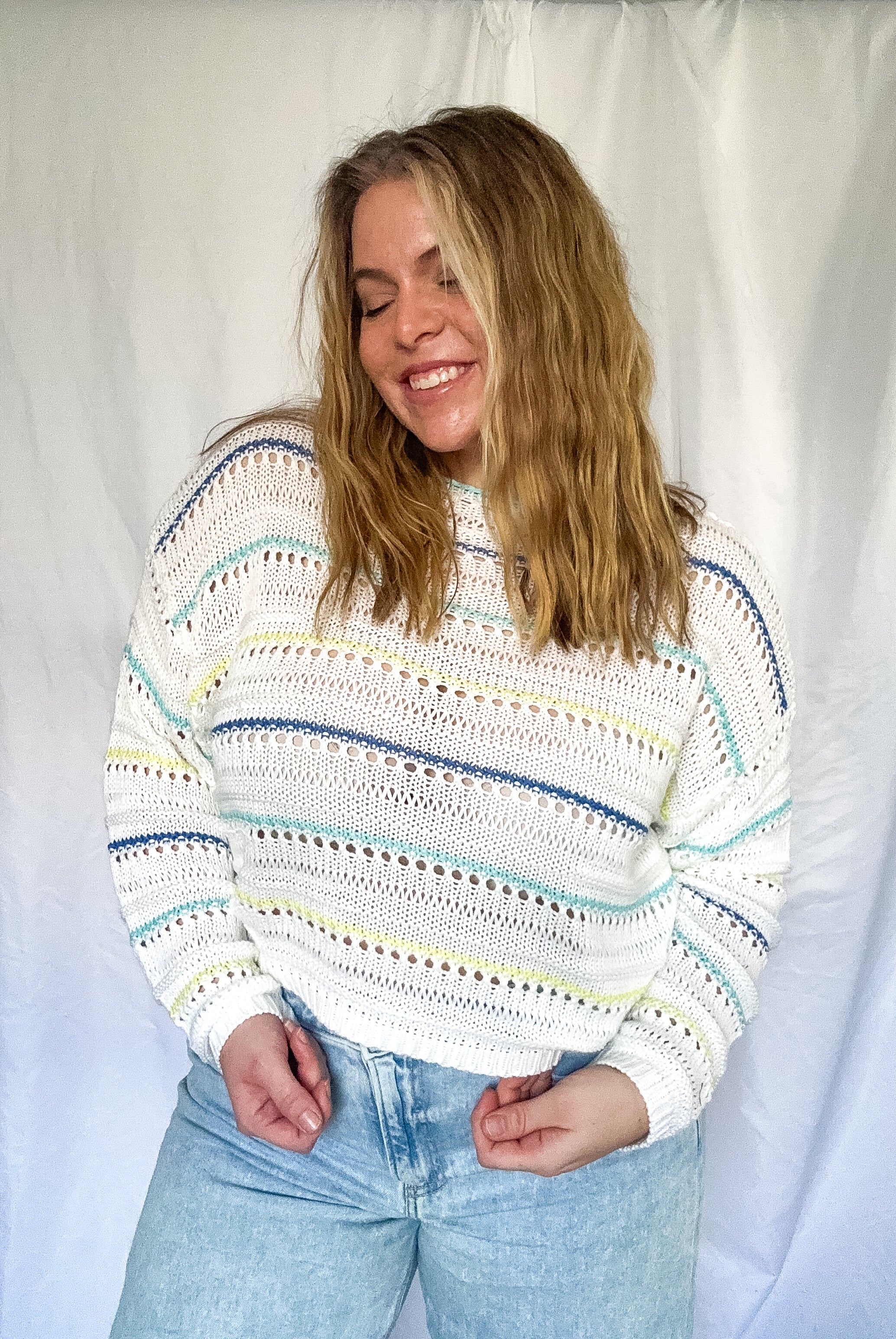 A white crochet sweater with blue, teal, and green stripes, featuring a pointelle design and relaxed fit.