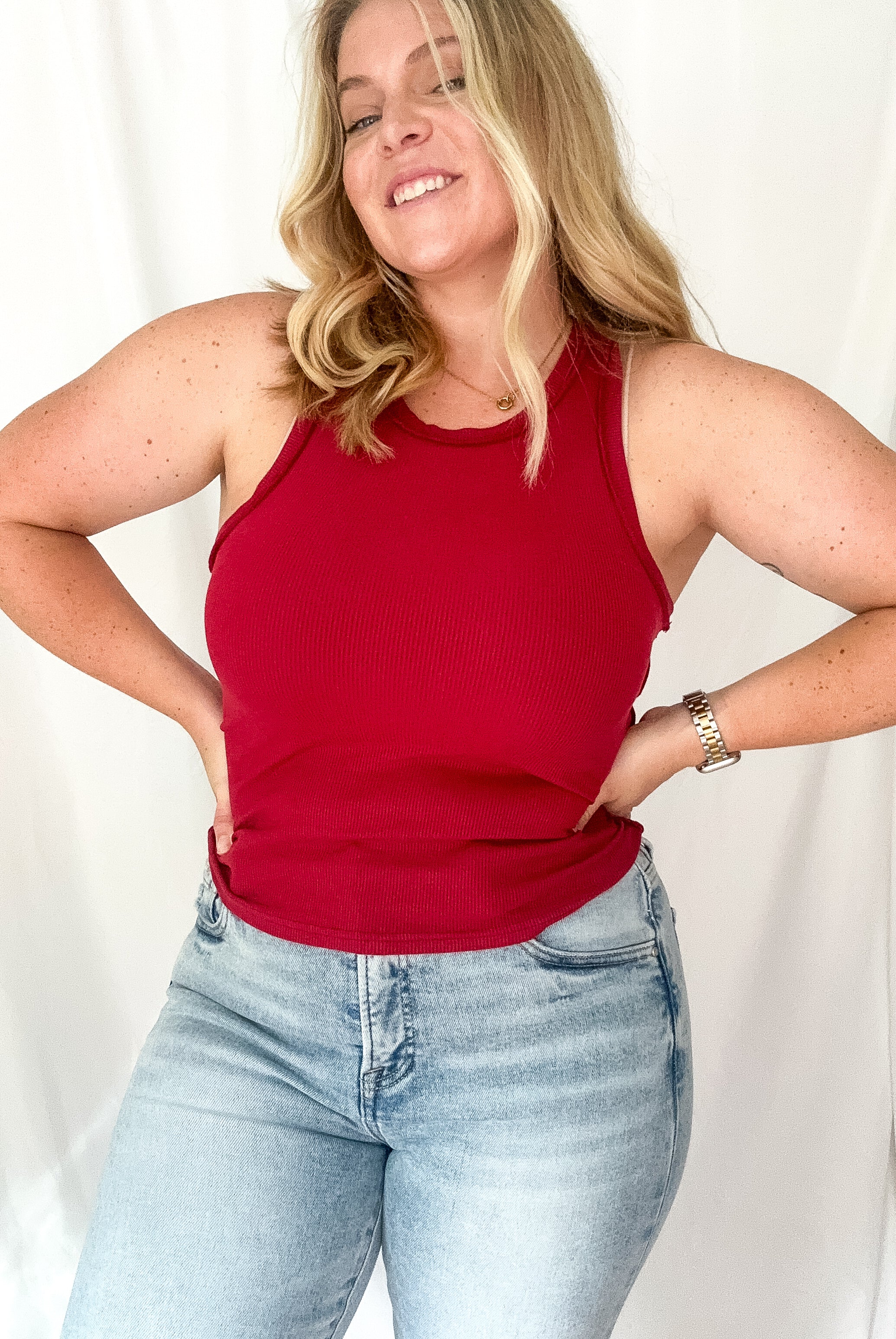 A woman wearing a burgundy ribbed tank with a round neckline, paired with light blue jeans.