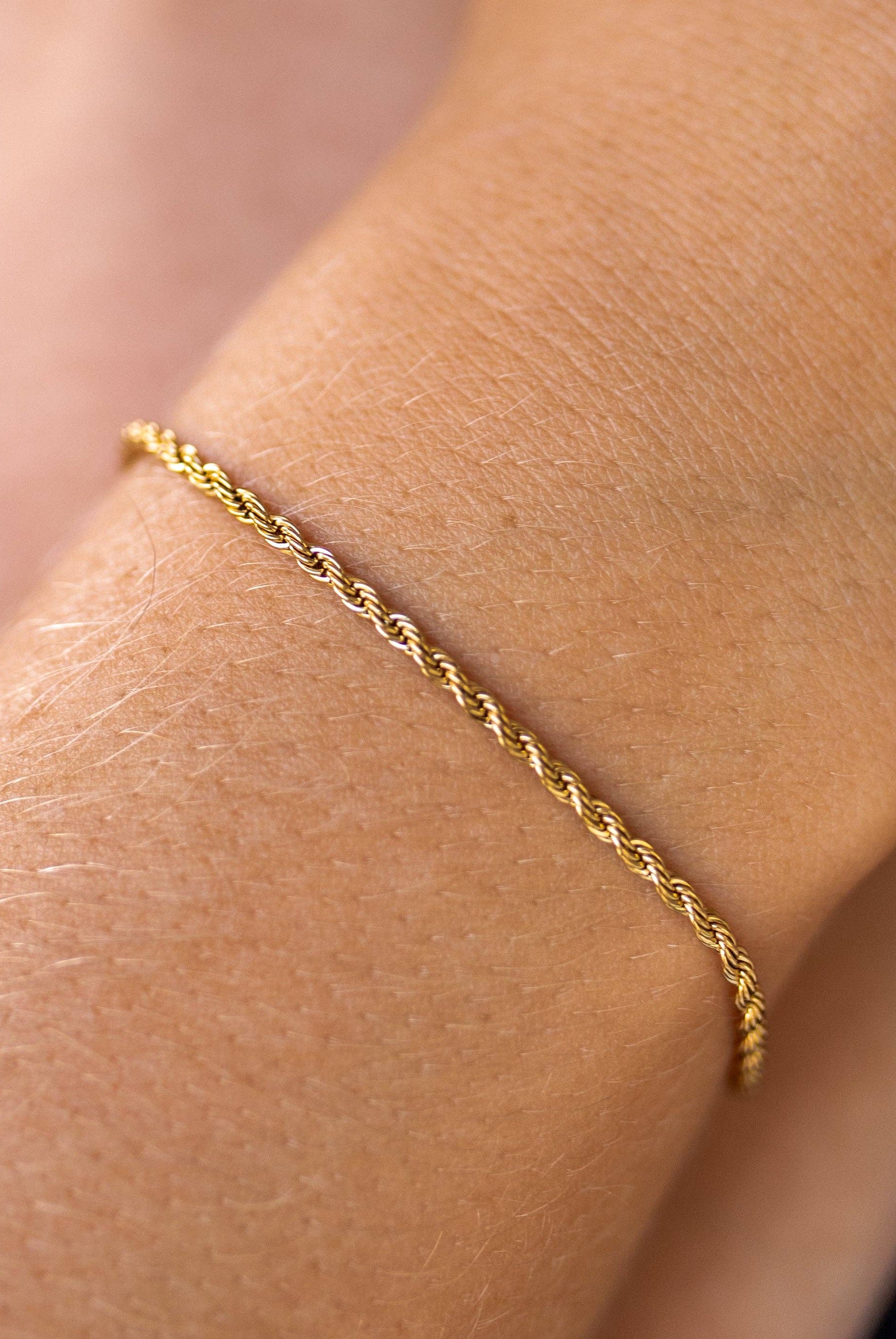 A delicate gold chain bracelet worn on a wrist, featuring a lobster clasp closure.