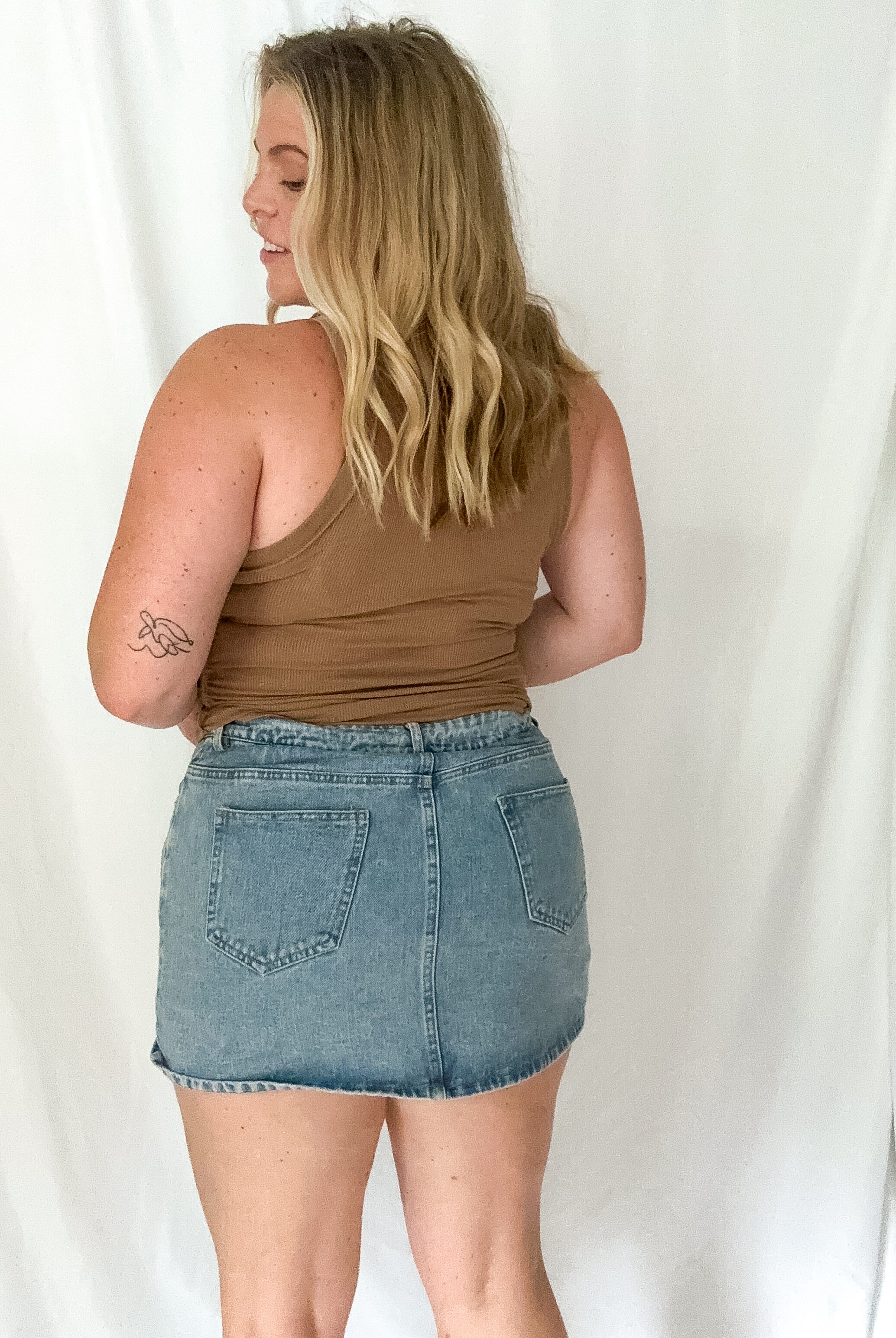 Woman wearing a brown tank top and denim skirt against a white background