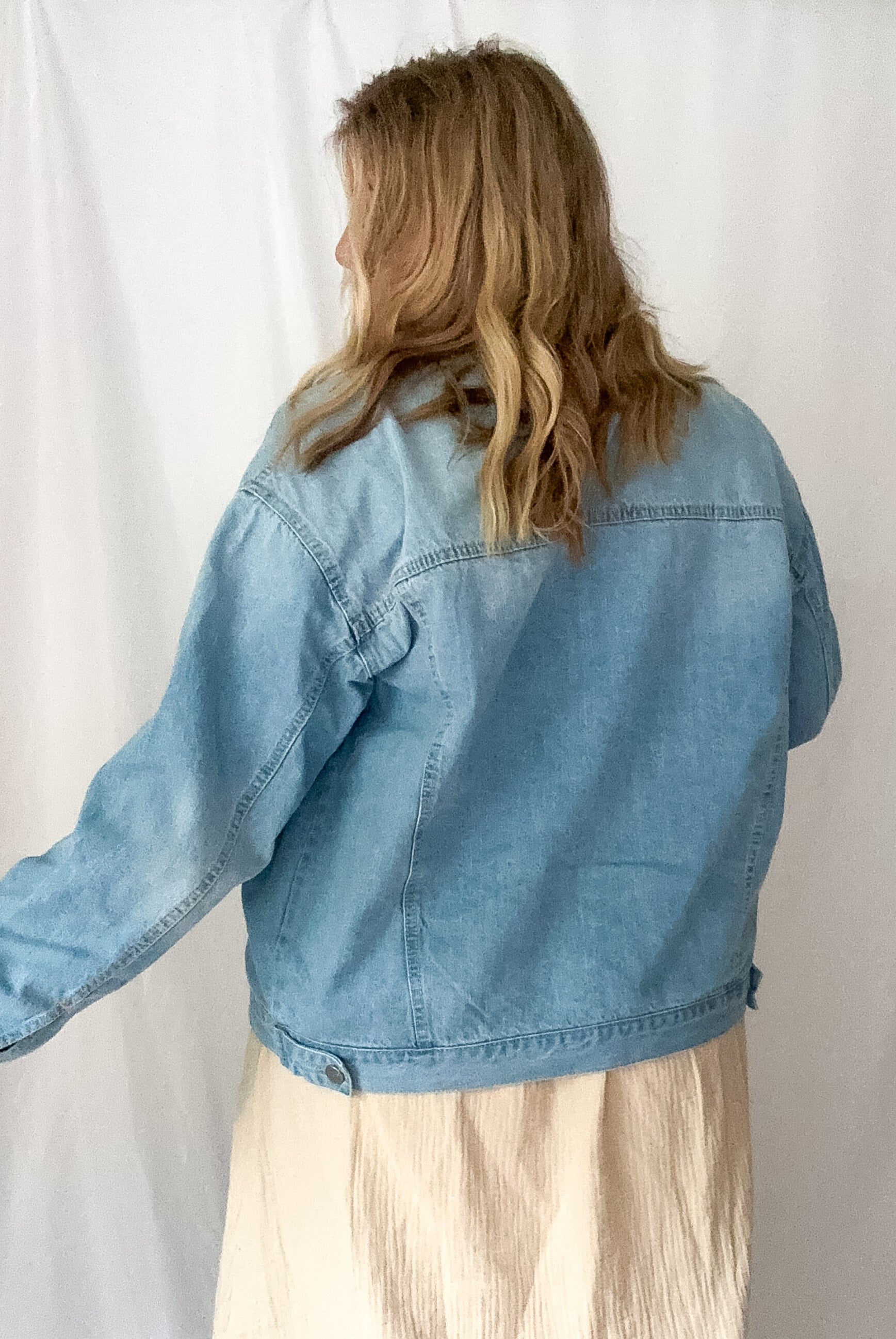 Person wearing a light blue denim jacket against a white background