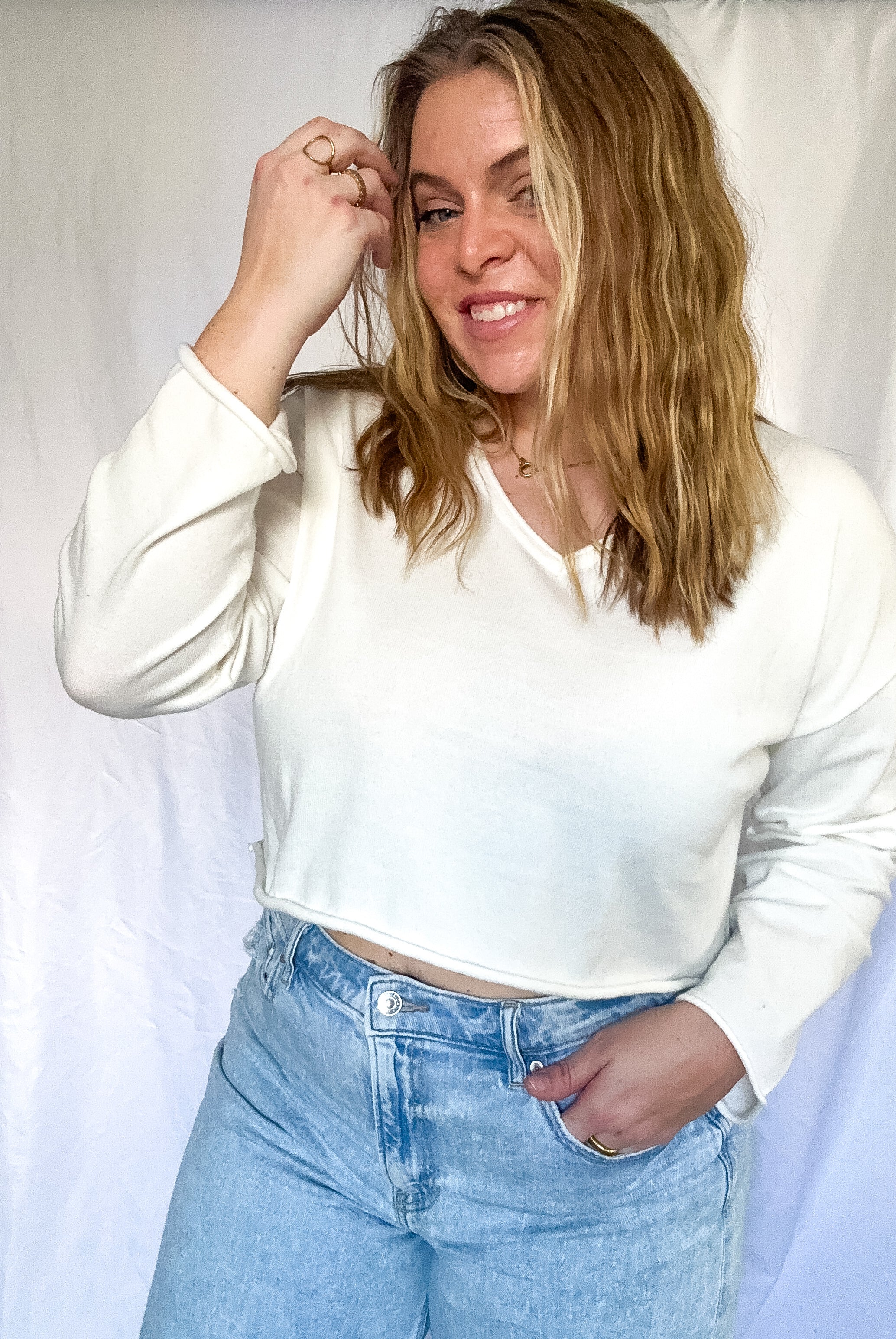 White cropped sweater with V-neckline and long sleeves, worn by a person.