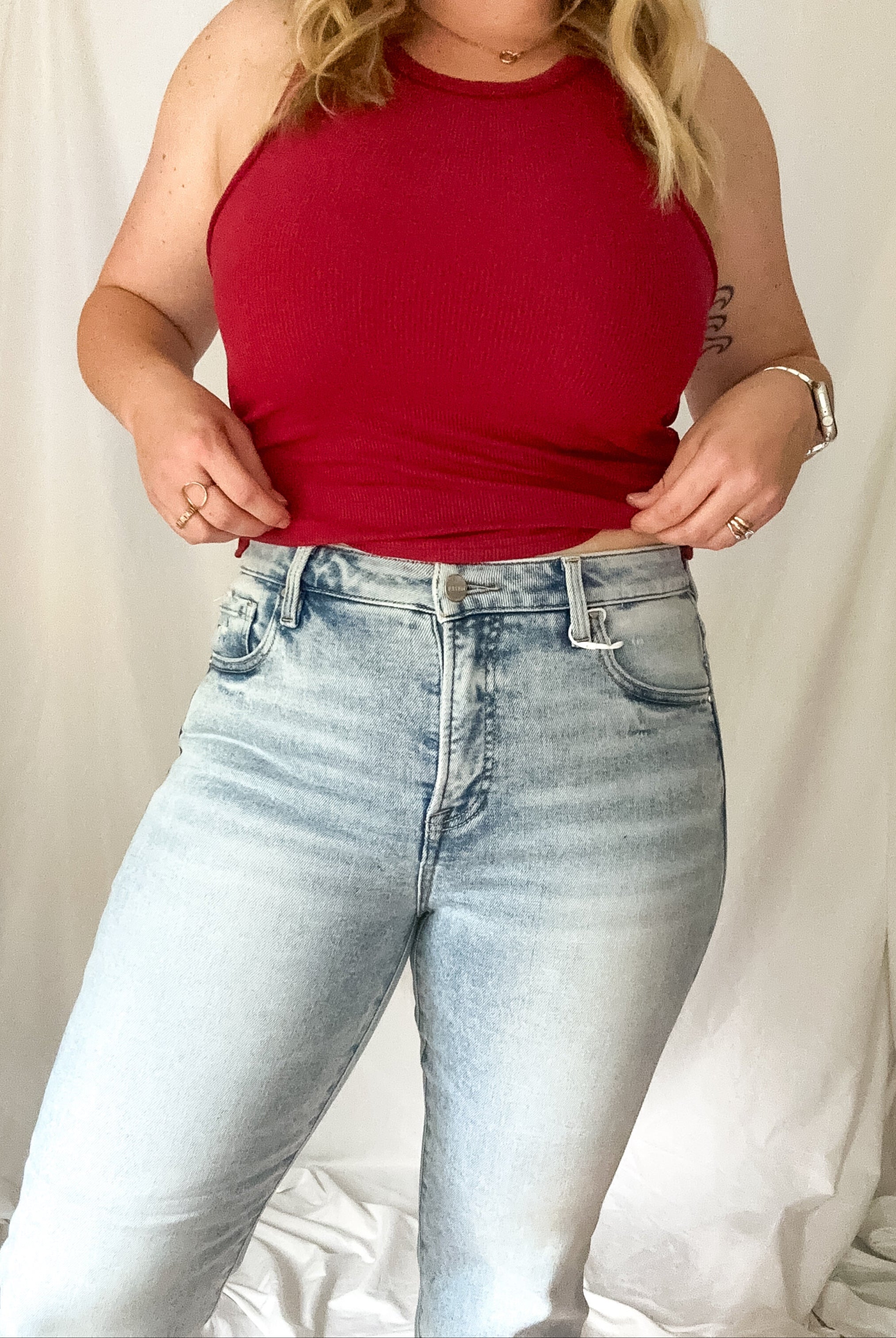 Person wearing a red tank top and light blue jeans against a plain background