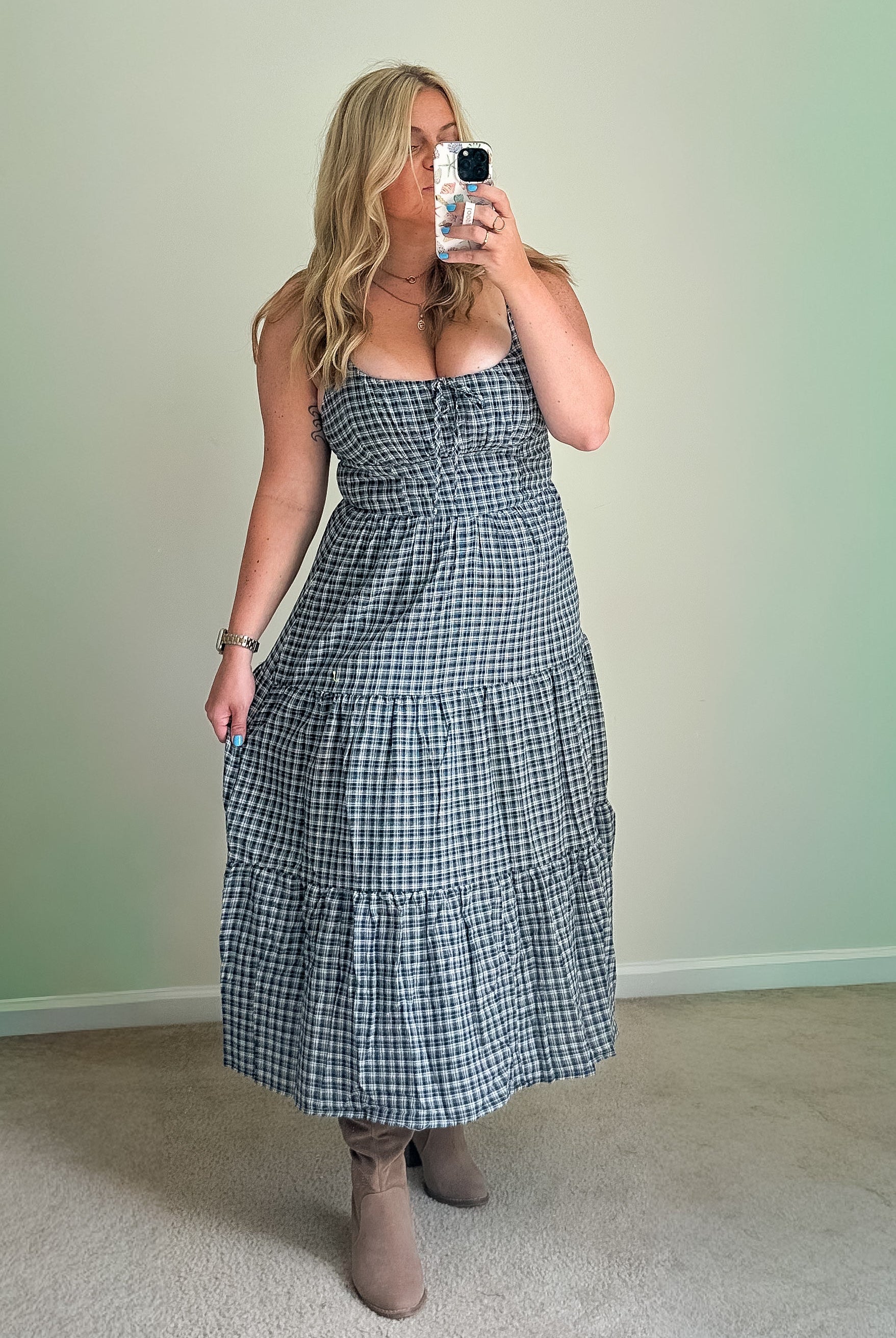 A woman wearing a blue plaid midi dress with a scoop neckline and adjustable straps, featuring a tiered skirt and front tie.