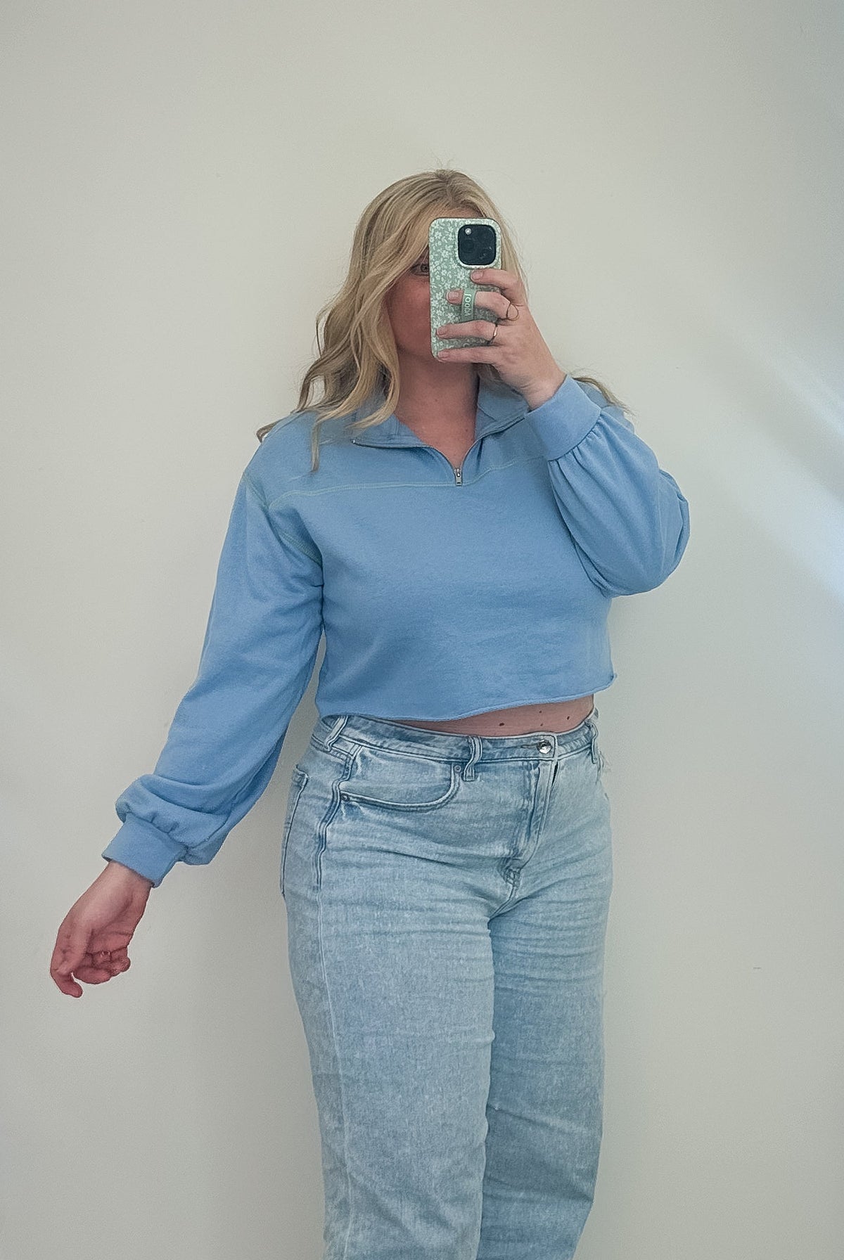 Person taking a mirror selfie wearing a blue top and light blue jeans in a room with a large mirror.