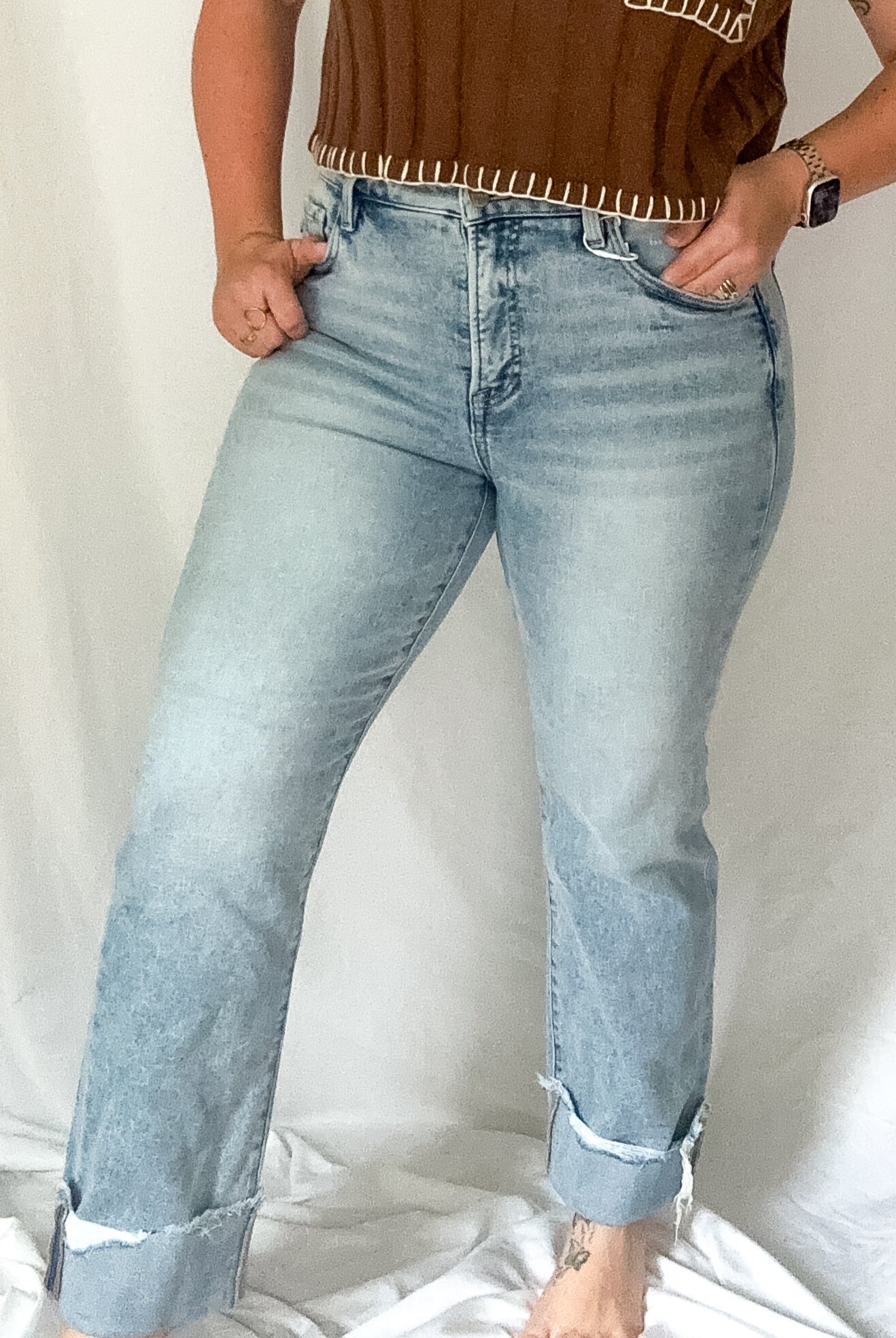 Woman wearing a brown top with fringe details and light blue jeans against a white background