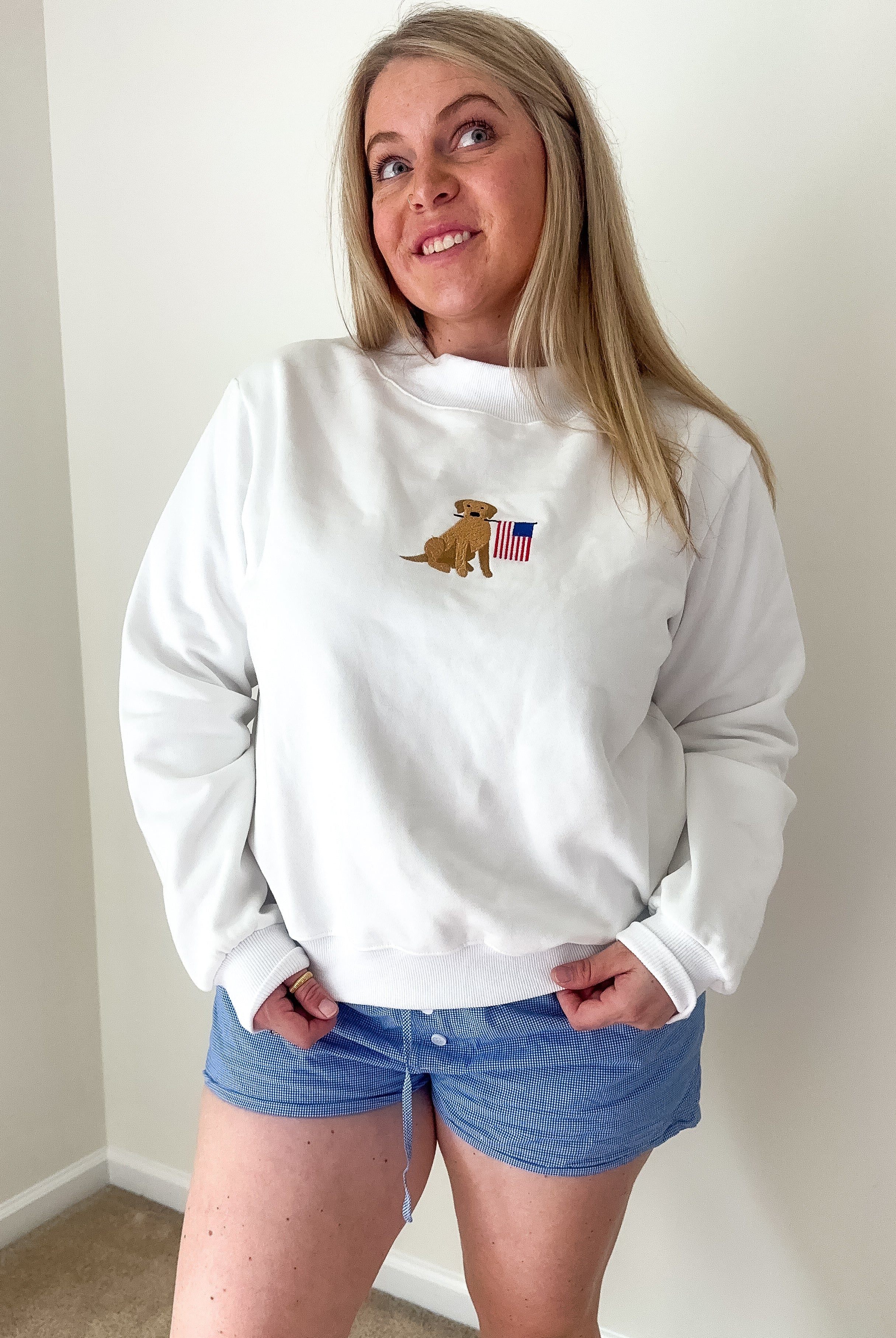 Person wearing a white sweatshirt with a logo and blue shorts indoors.