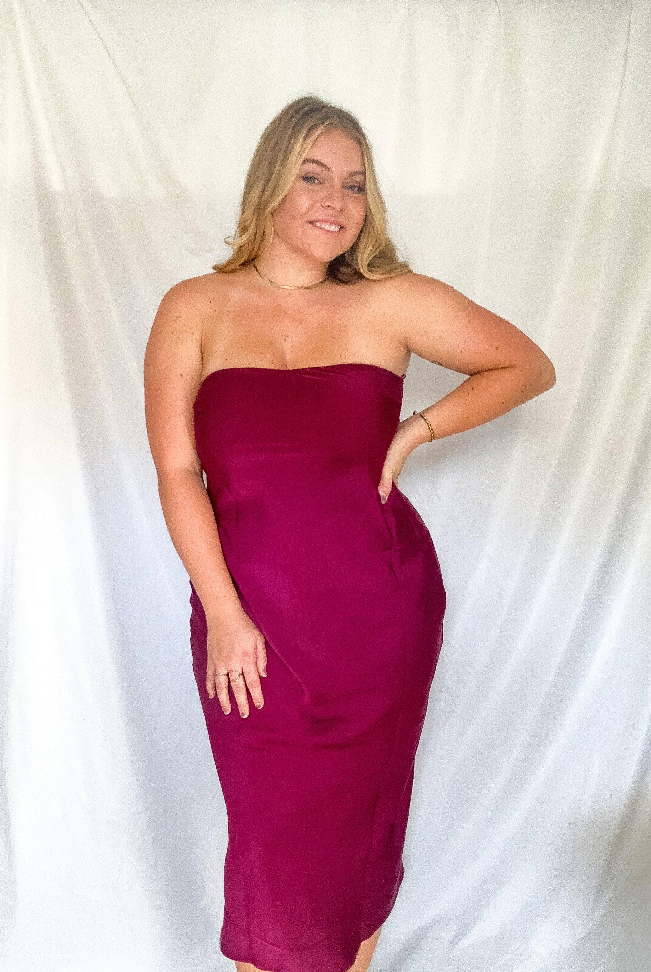 A strapless midi dress in wine with a cowl back detail, worn by a model.