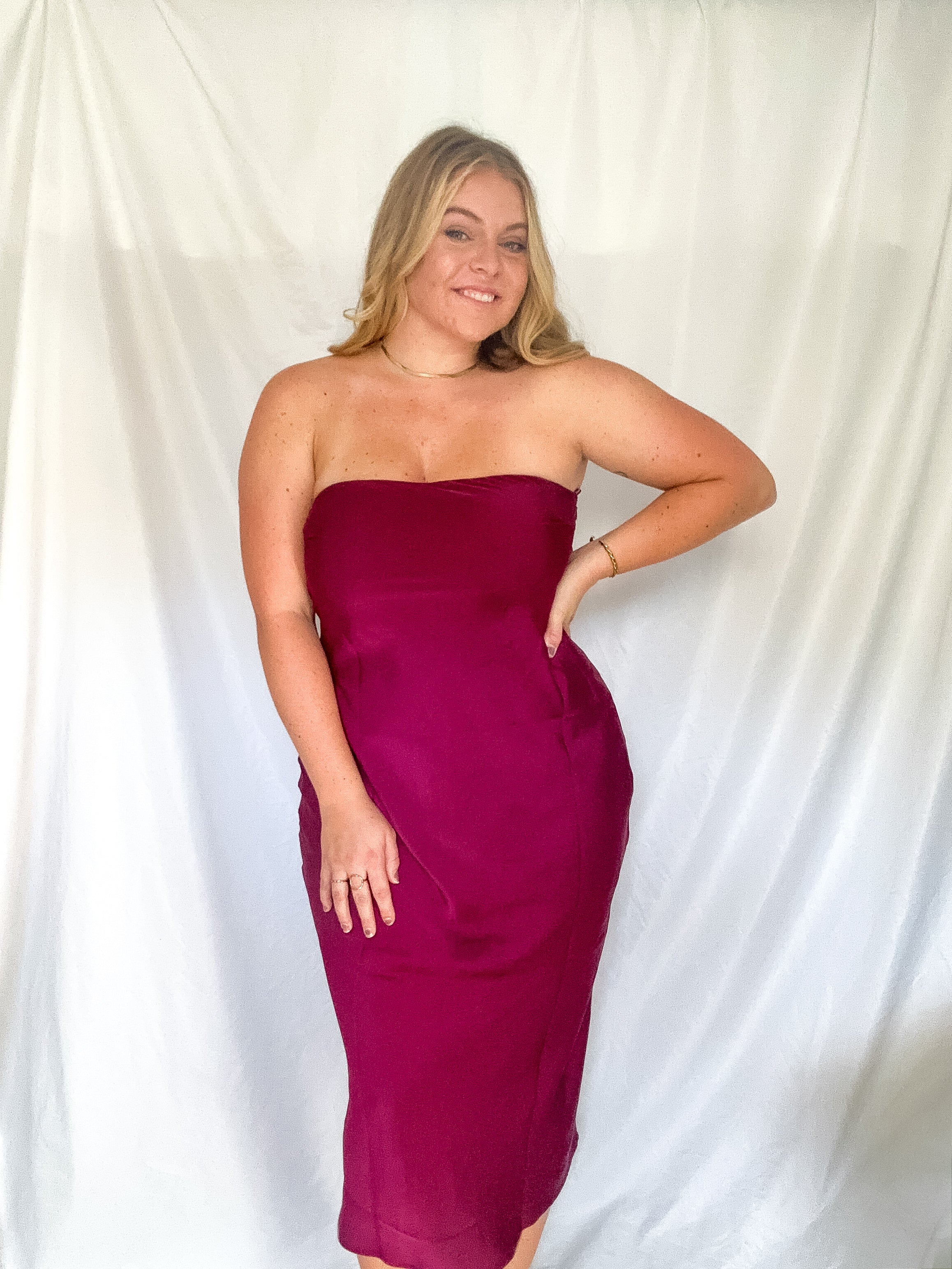 A strapless midi dress in wine with a cowl back detail, worn by a model.