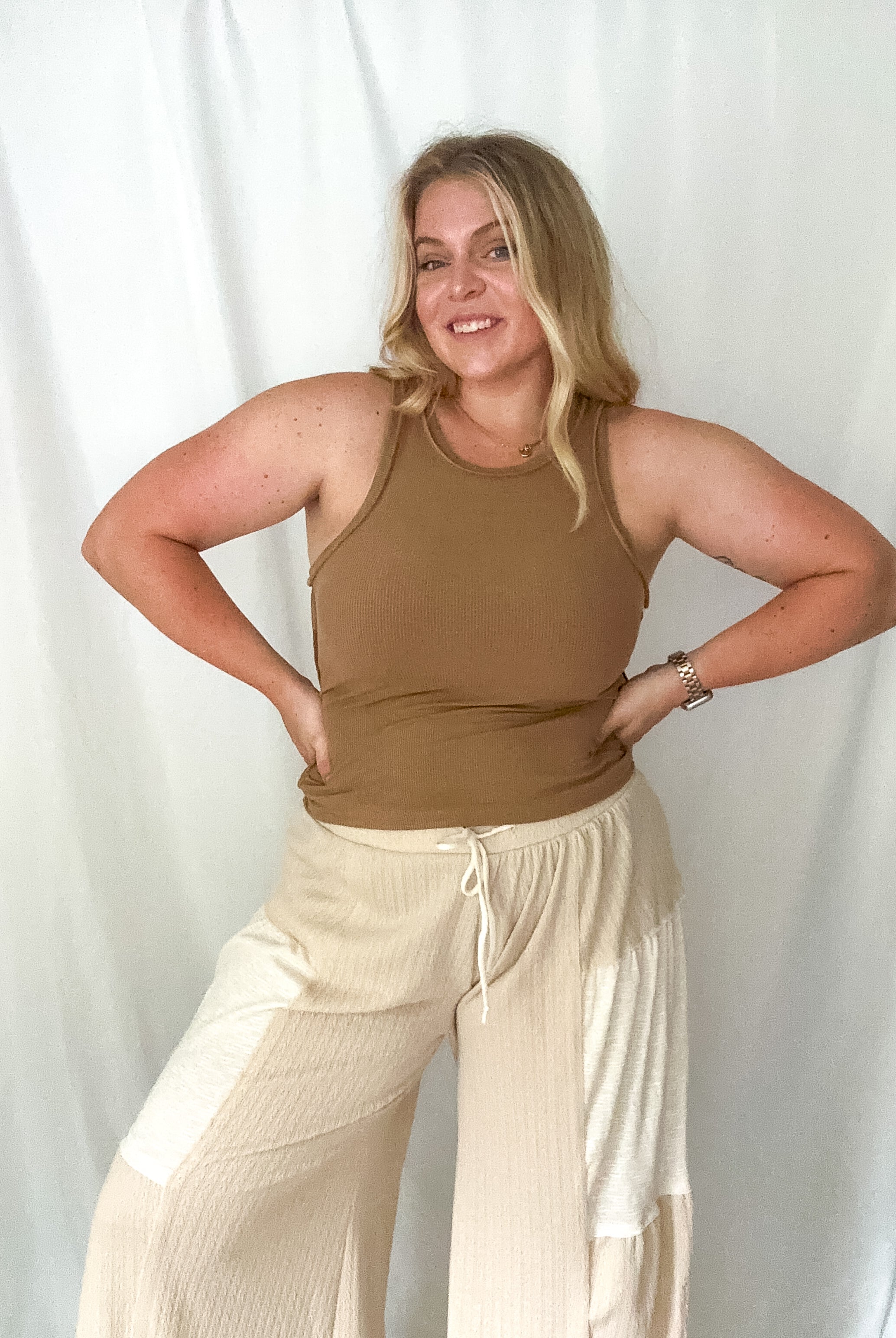 A woman wearing a tan ribbed tank with a round neckline.