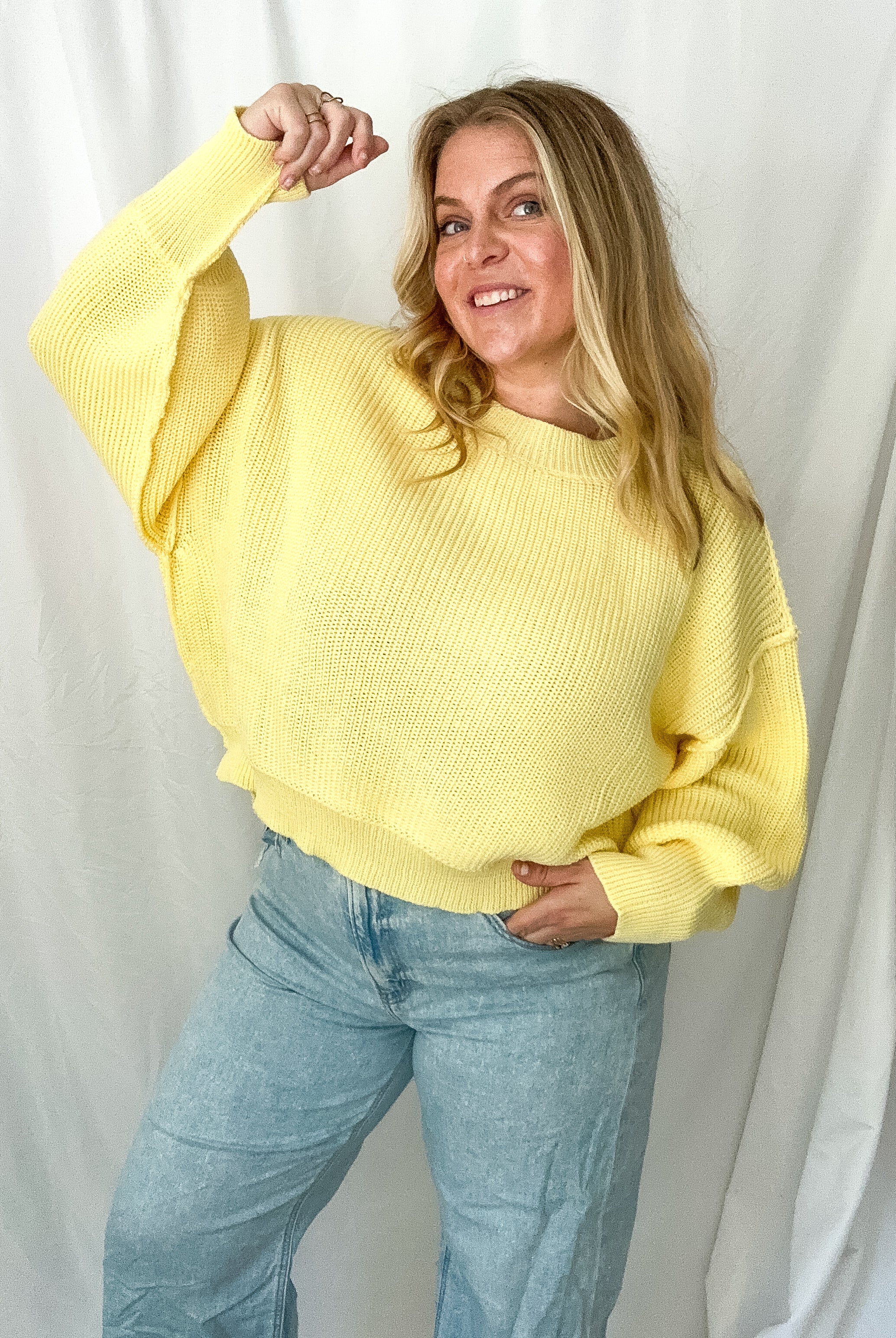 Person wearing a yellow sweater and light blue jeans against a white background