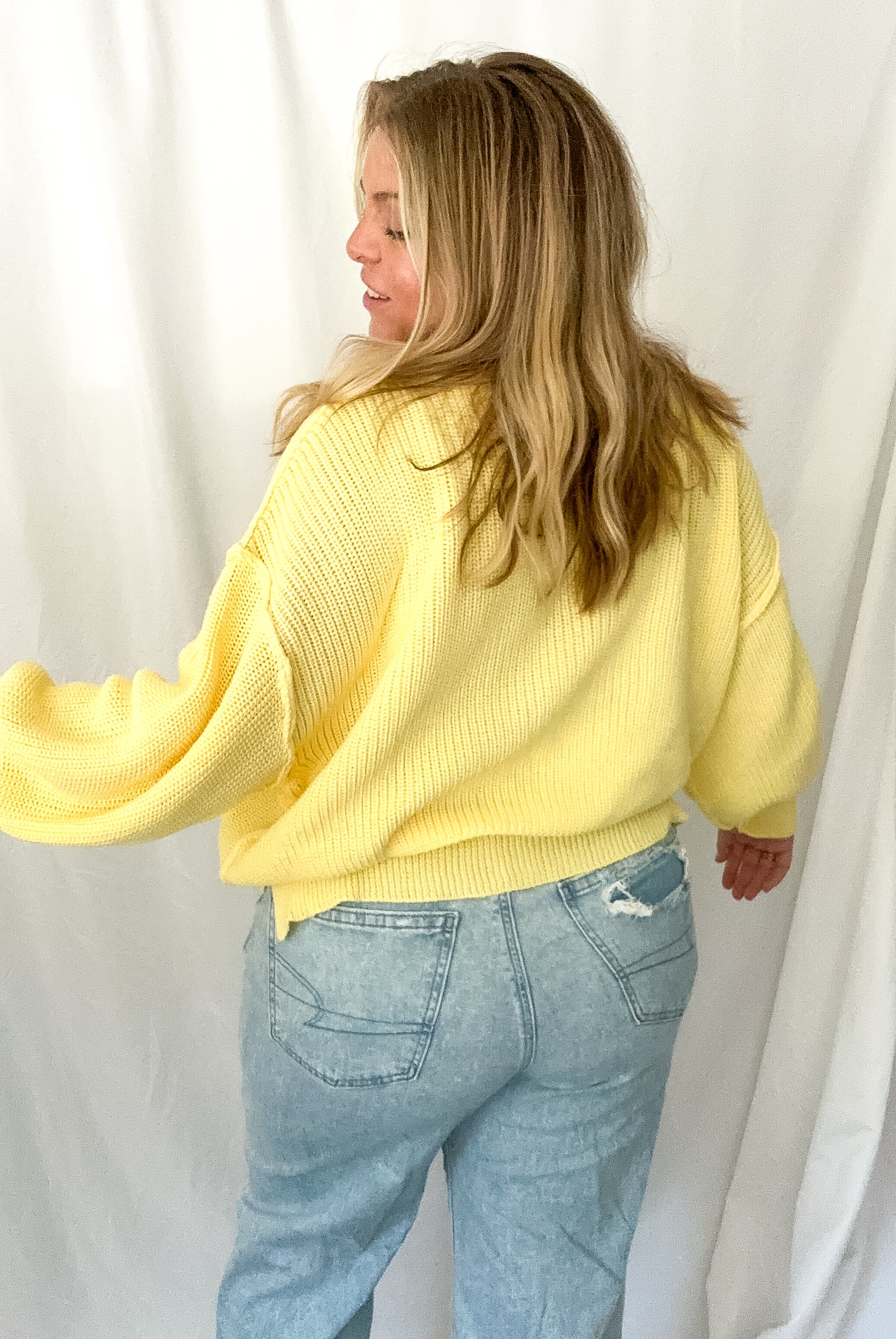 Person wearing a yellow sweater and light blue jeans against a white background