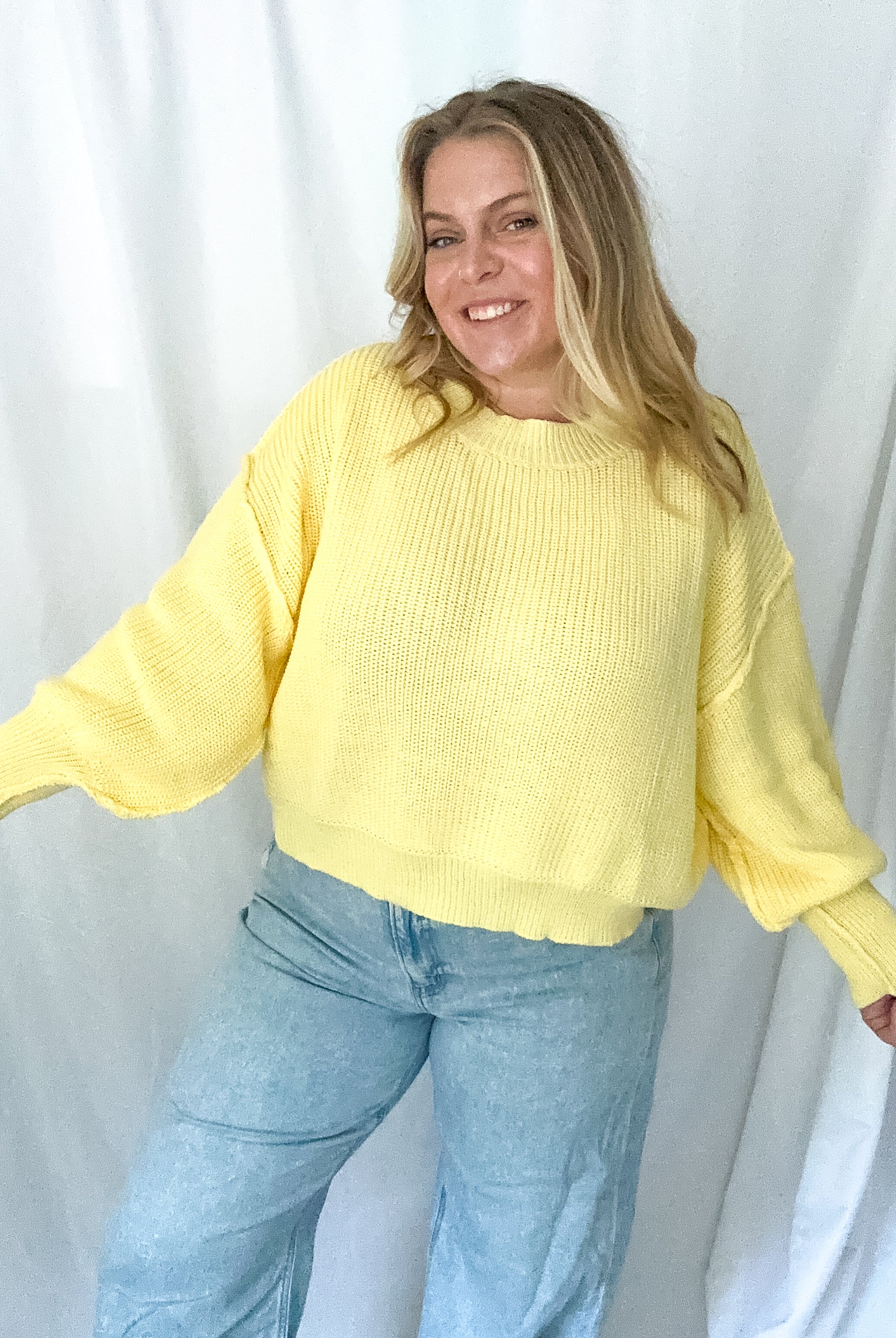Person wearing a yellow sweater and blue jeans against a white background