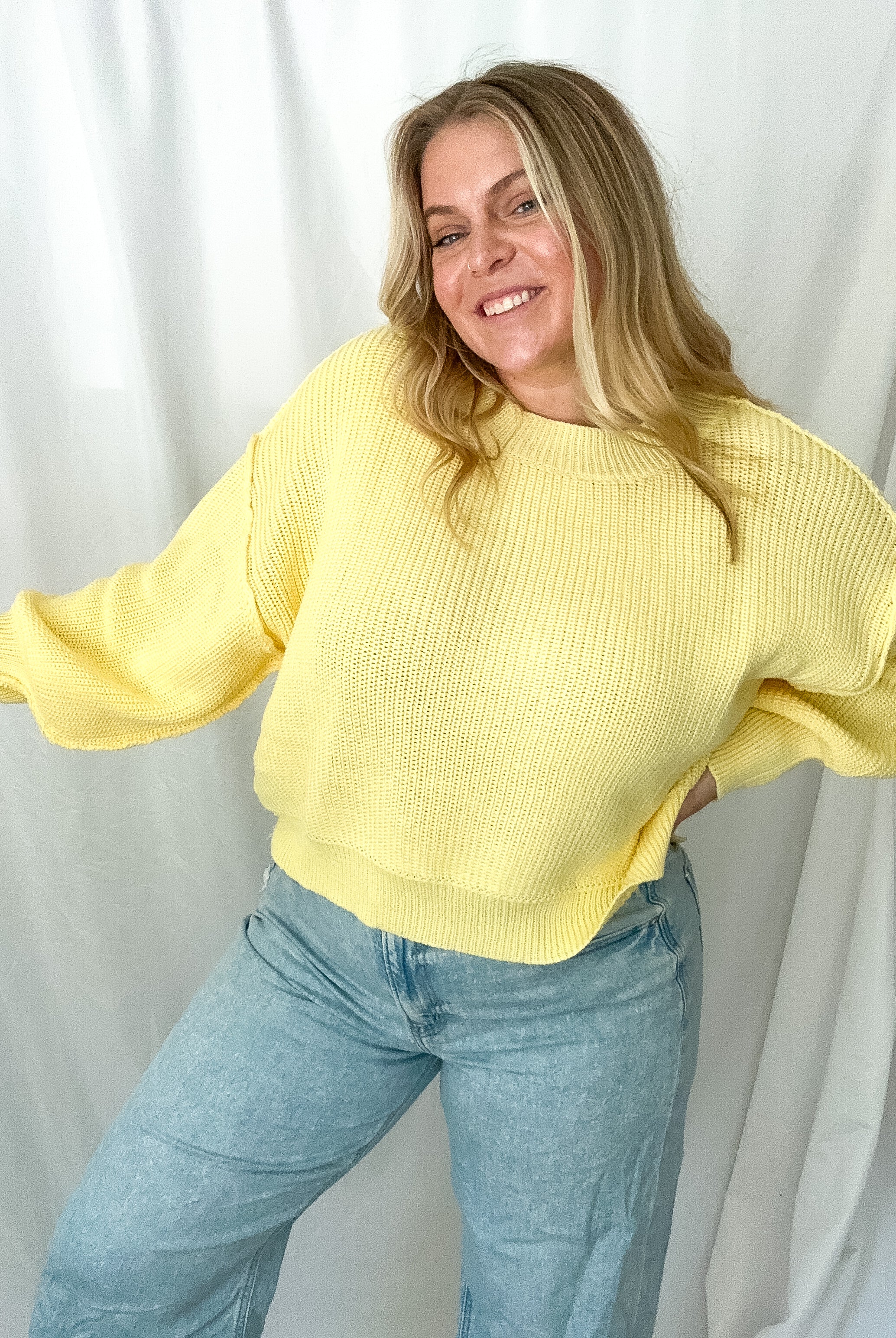 Yellow knit sweater with a mock neckline and relaxed fit, worn by a person with light-wash jeans.