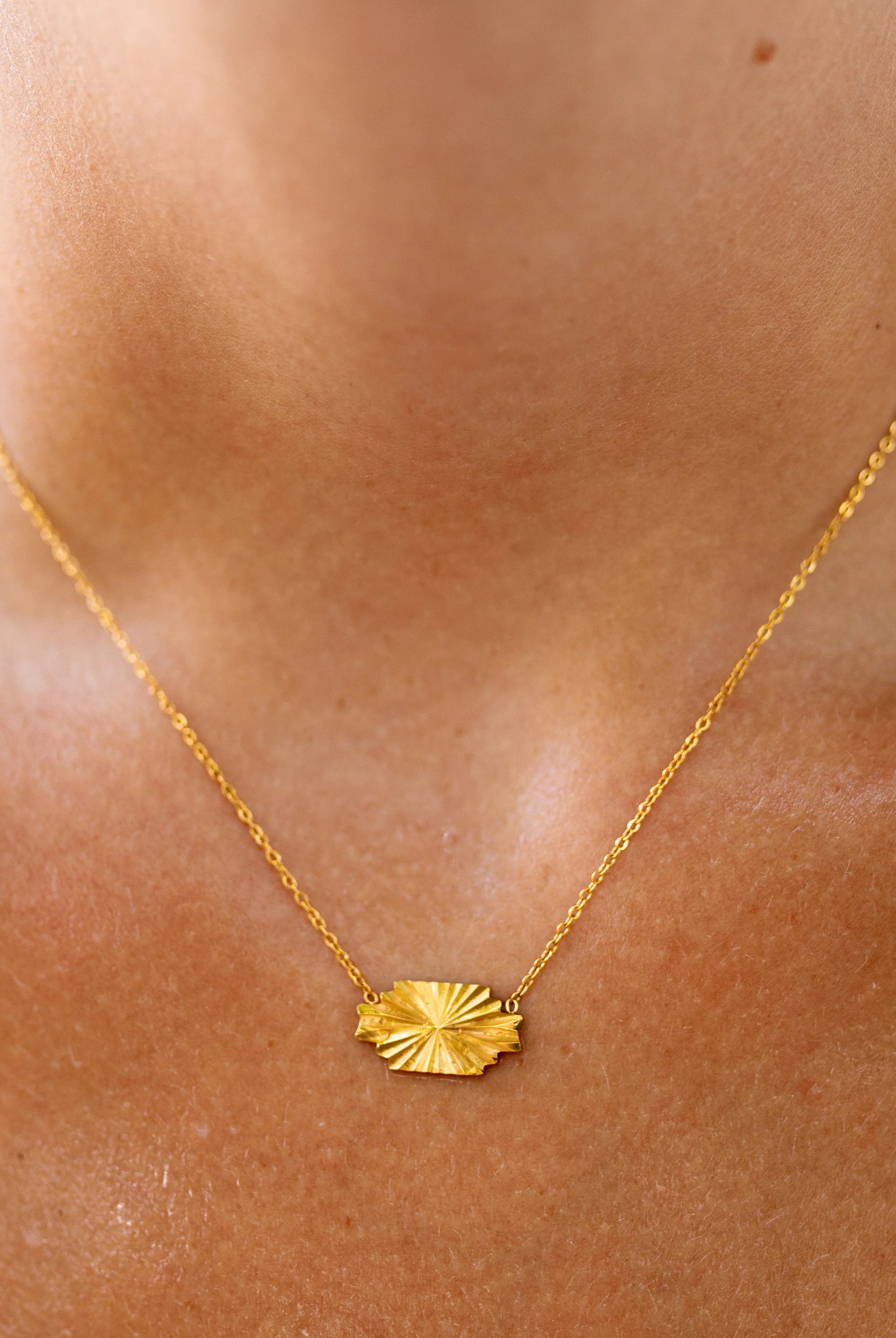 Gold necklace with a leaf pendant on a person's neck
