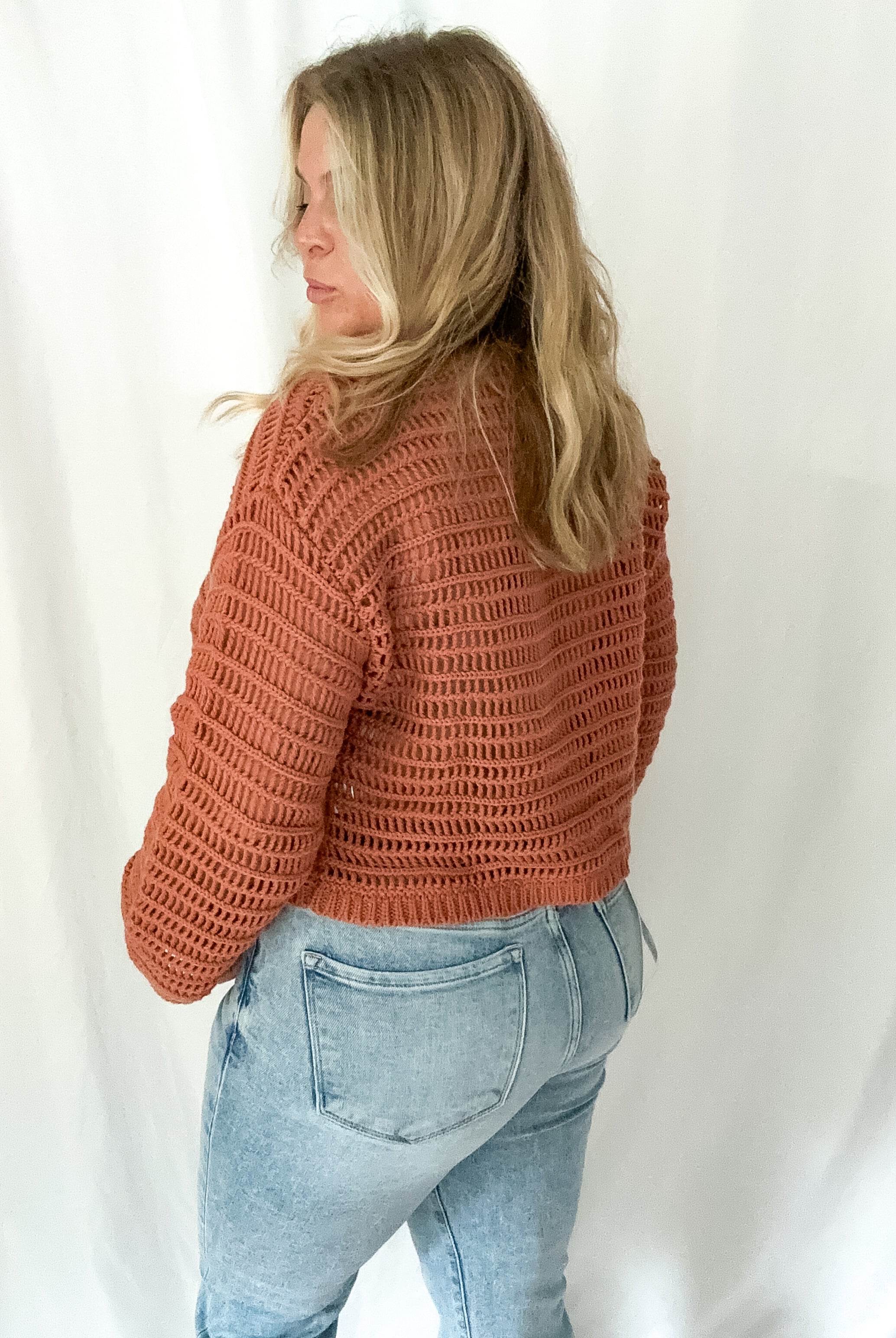 Person wearing a brown knitted sweater and light blue jeans against a white background