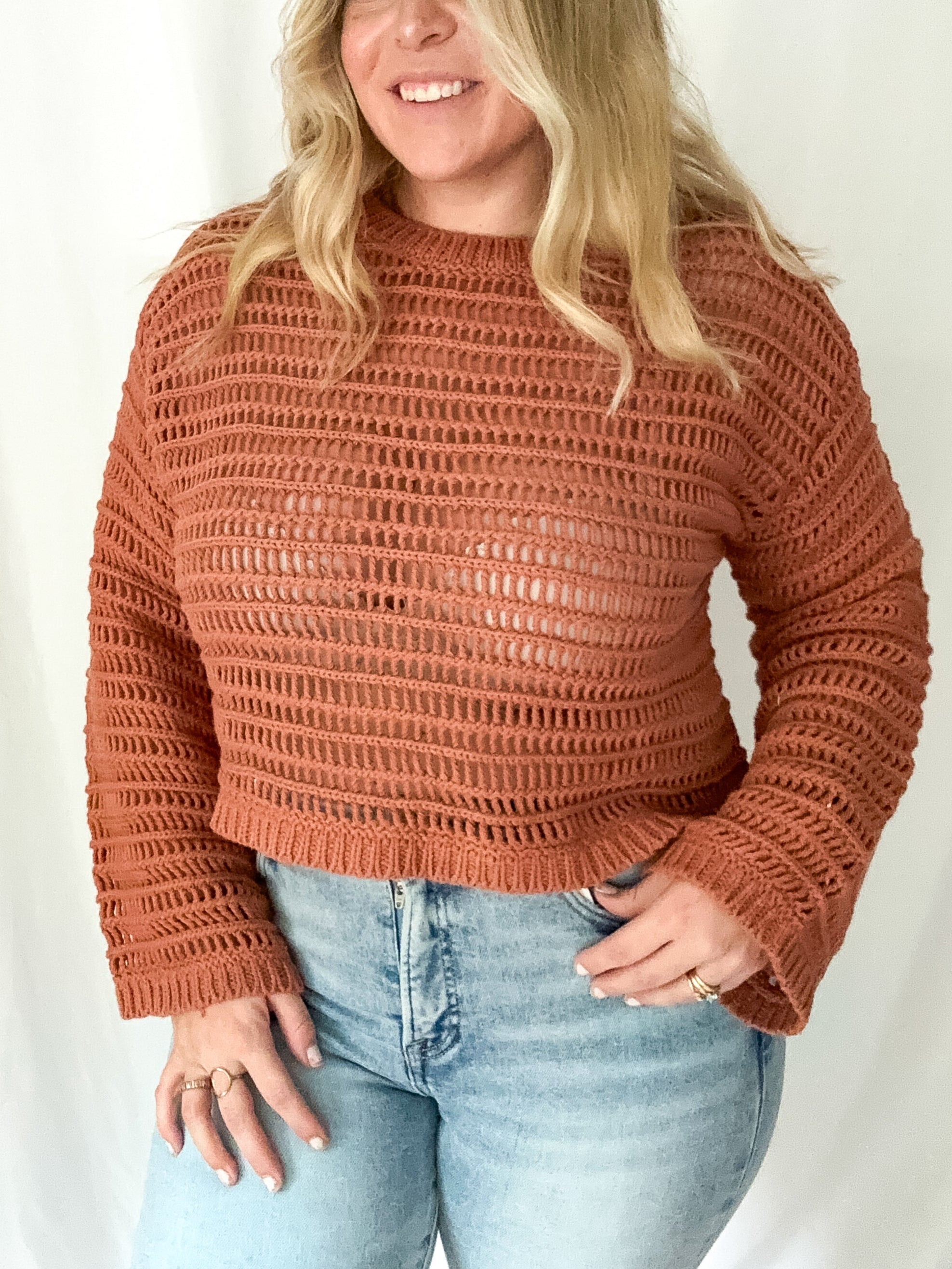 Woman wearing a brown knitted sweater and light blue jeans against a white background