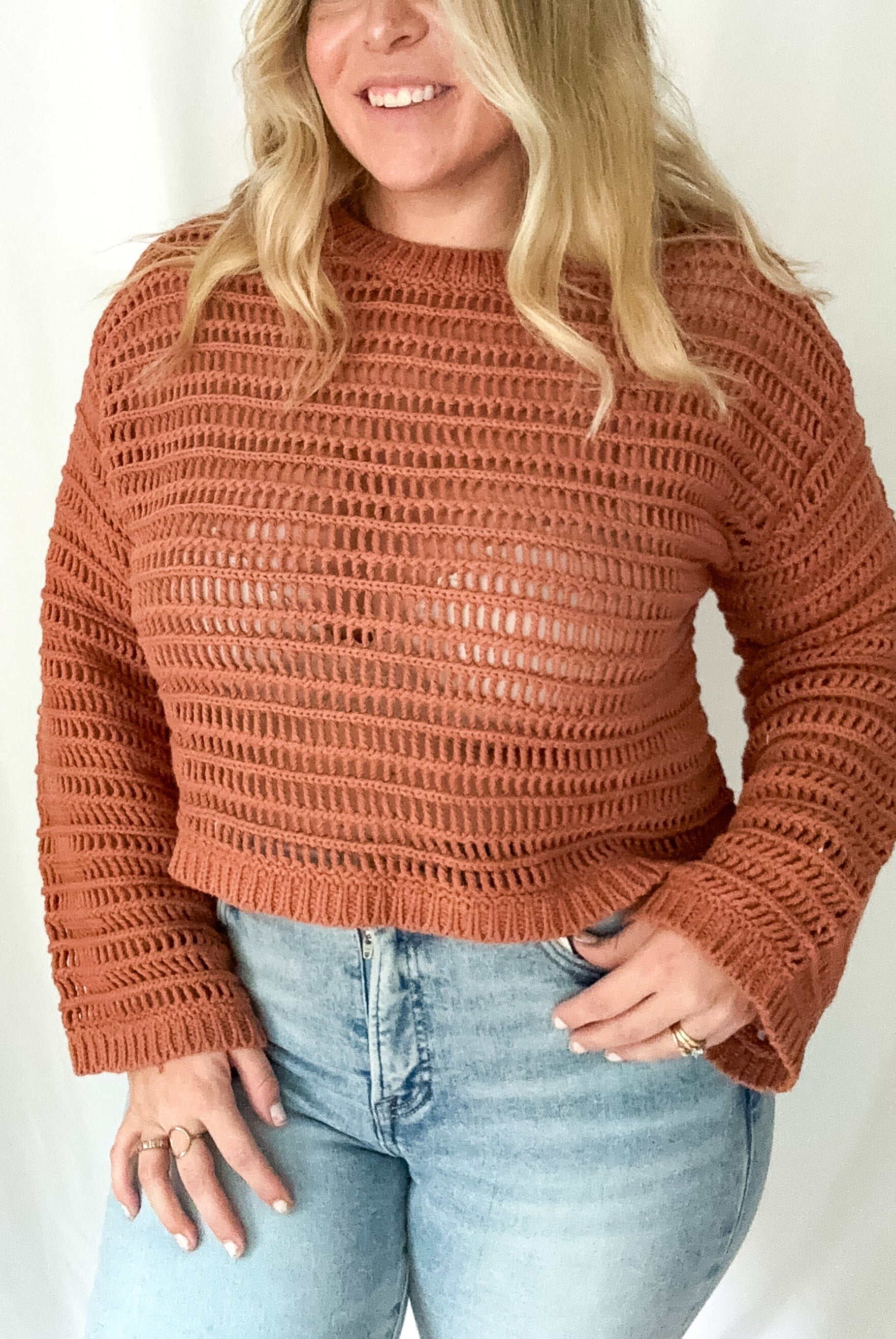 Woman wearing a brown knitted sweater and light blue jeans against a white background