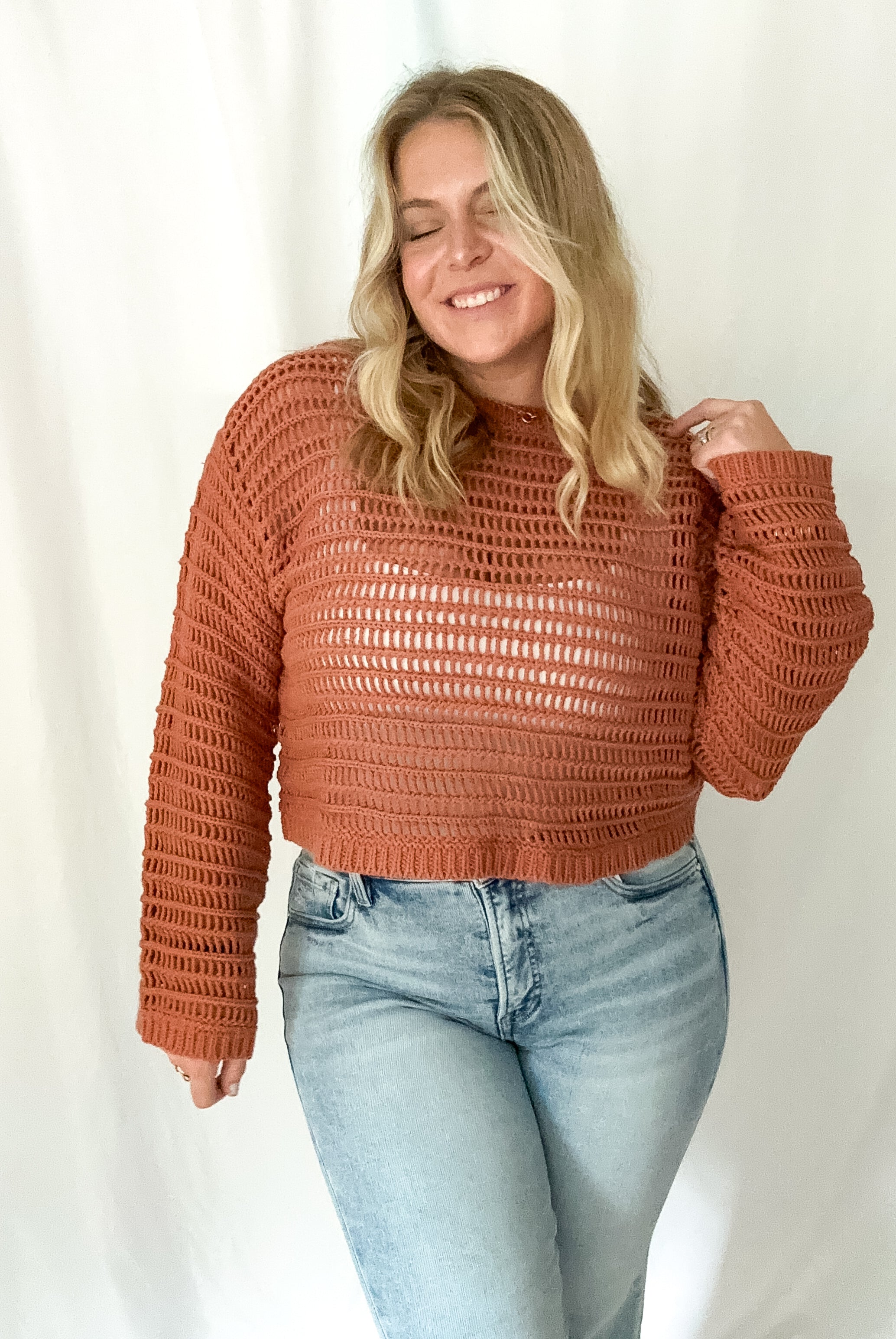 Woman wearing a brown textured sweater and light blue jeans against a white background