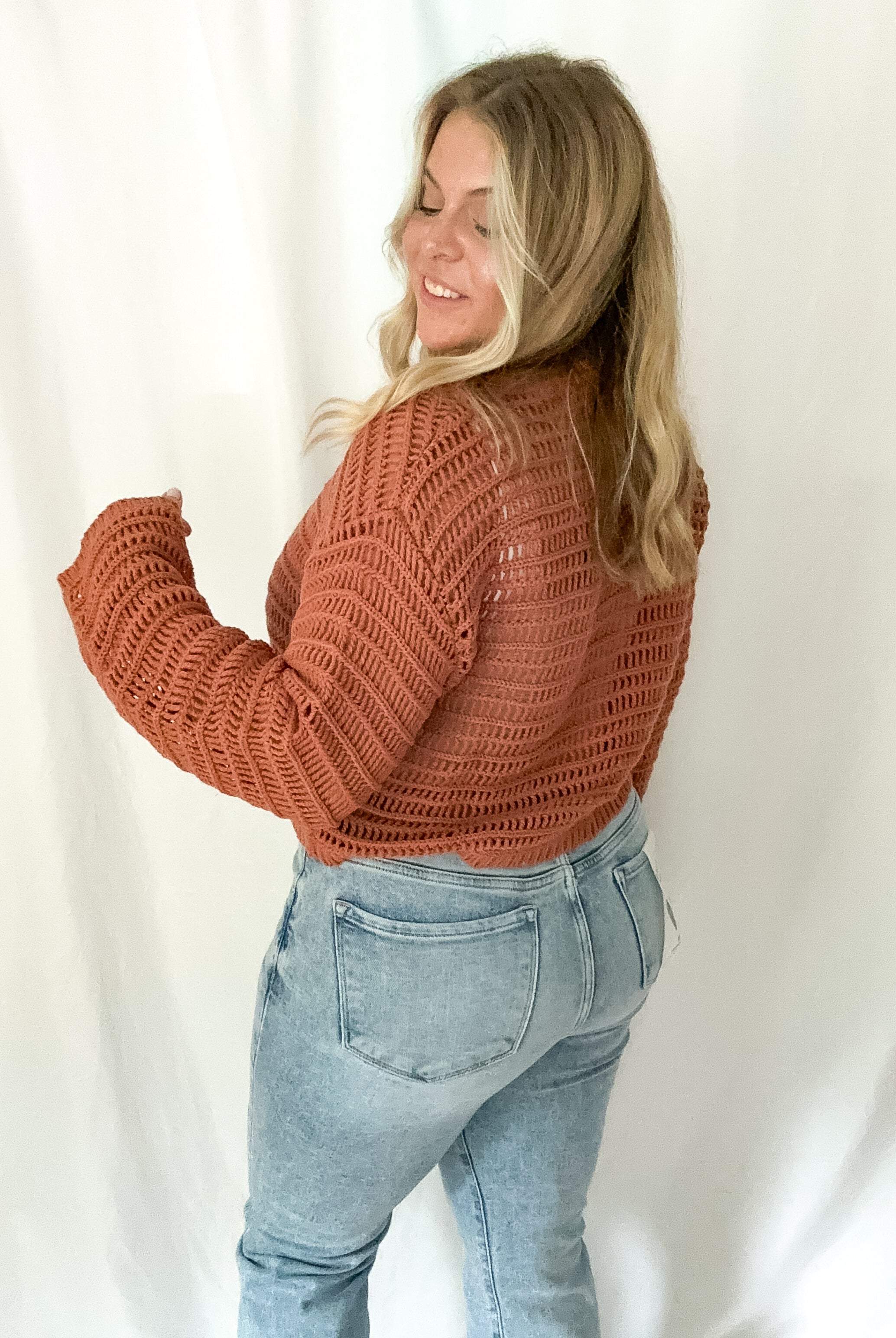 Woman wearing a brown knitted sweater and light blue jeans against a white background