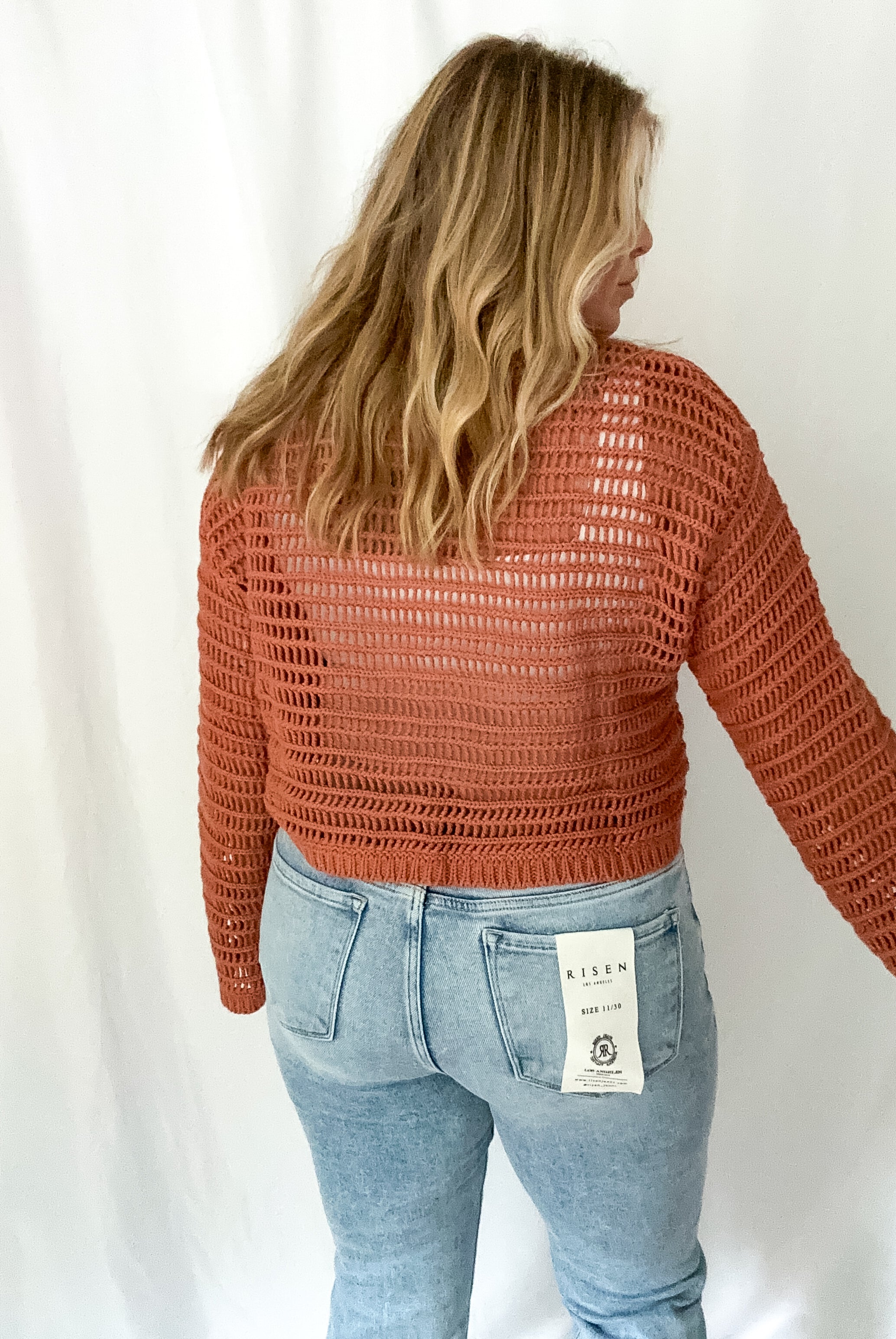 Person wearing a rust-colored knit sweater and light blue jeans with a white background