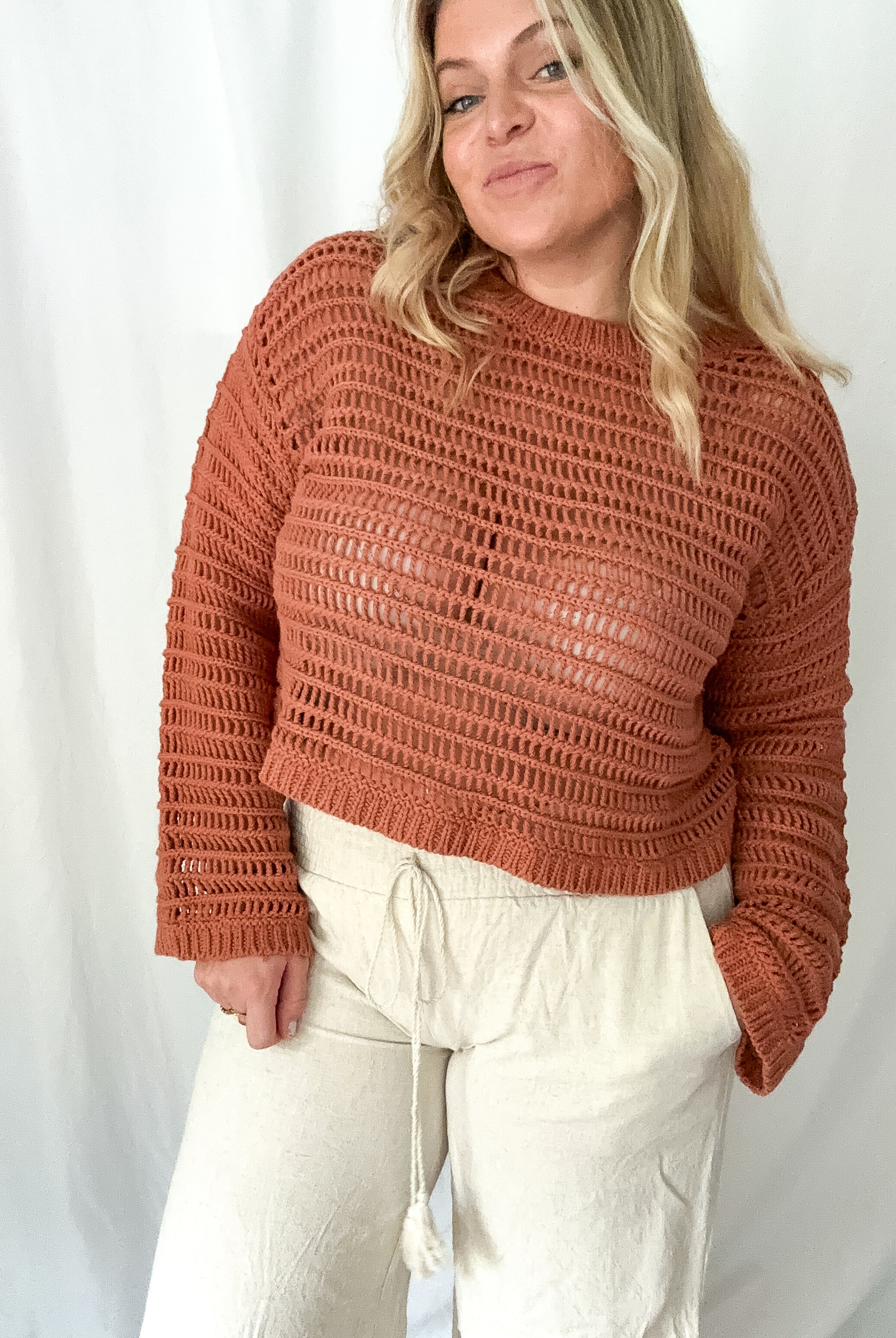 Person wearing a brown knitted sweater and white pants against a plain background