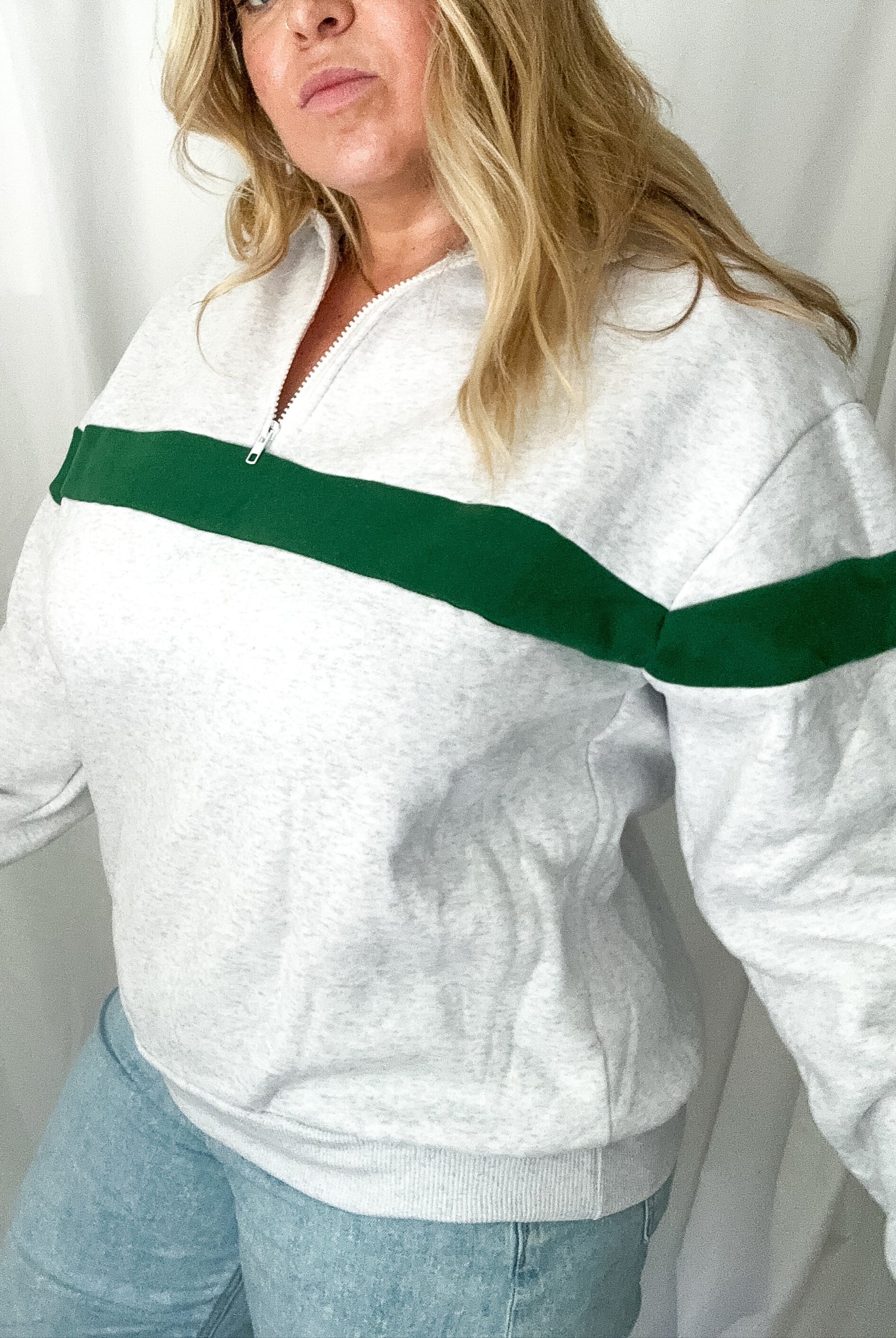 Woman wearing a white sweatshirt with a green stripe against a plain background