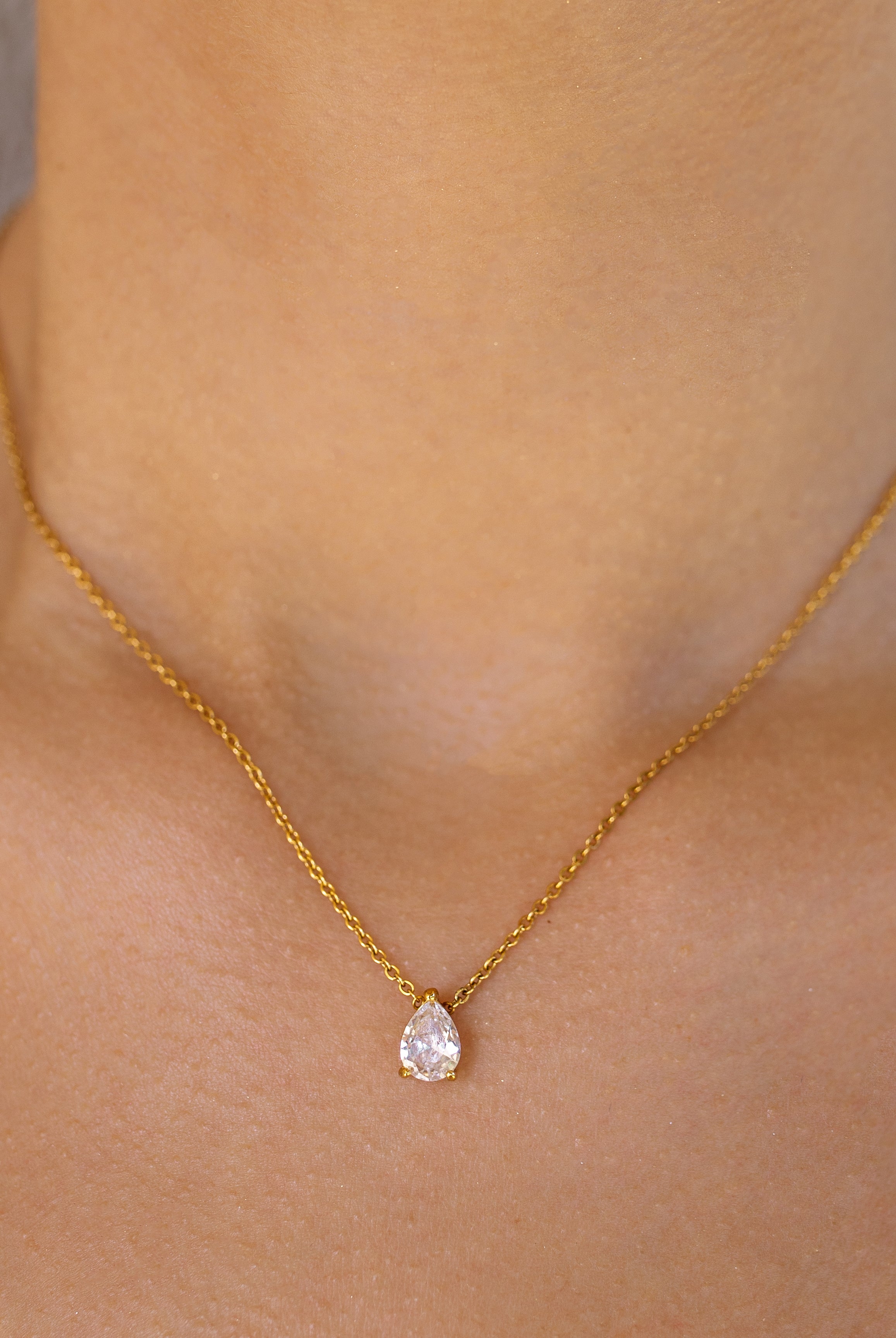 A delicate gold necklace with a pear-shaped pendant on a person's neck.
