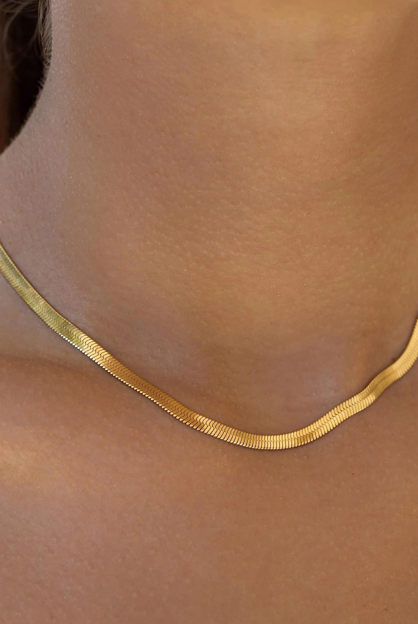 Gold necklace on a person's neck with a neutral background