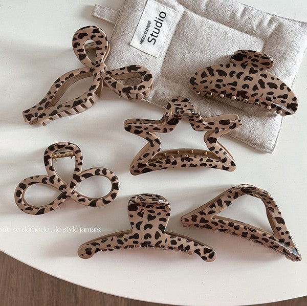 A collection of leopard print claw hair clips of various sizes displayed on a white surface with a leopard print bag in the background.
