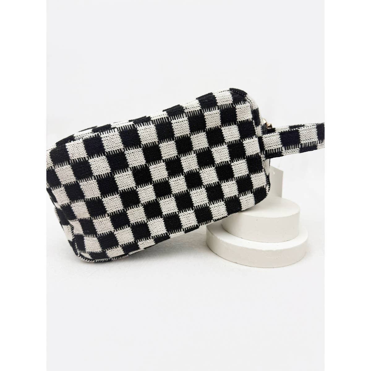 Checkered cosmetic bag in black and white with a handle and zipper closure.