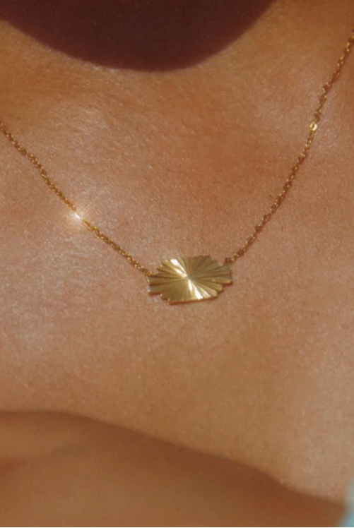 Gold necklace with a leaf pendant on a person's neck