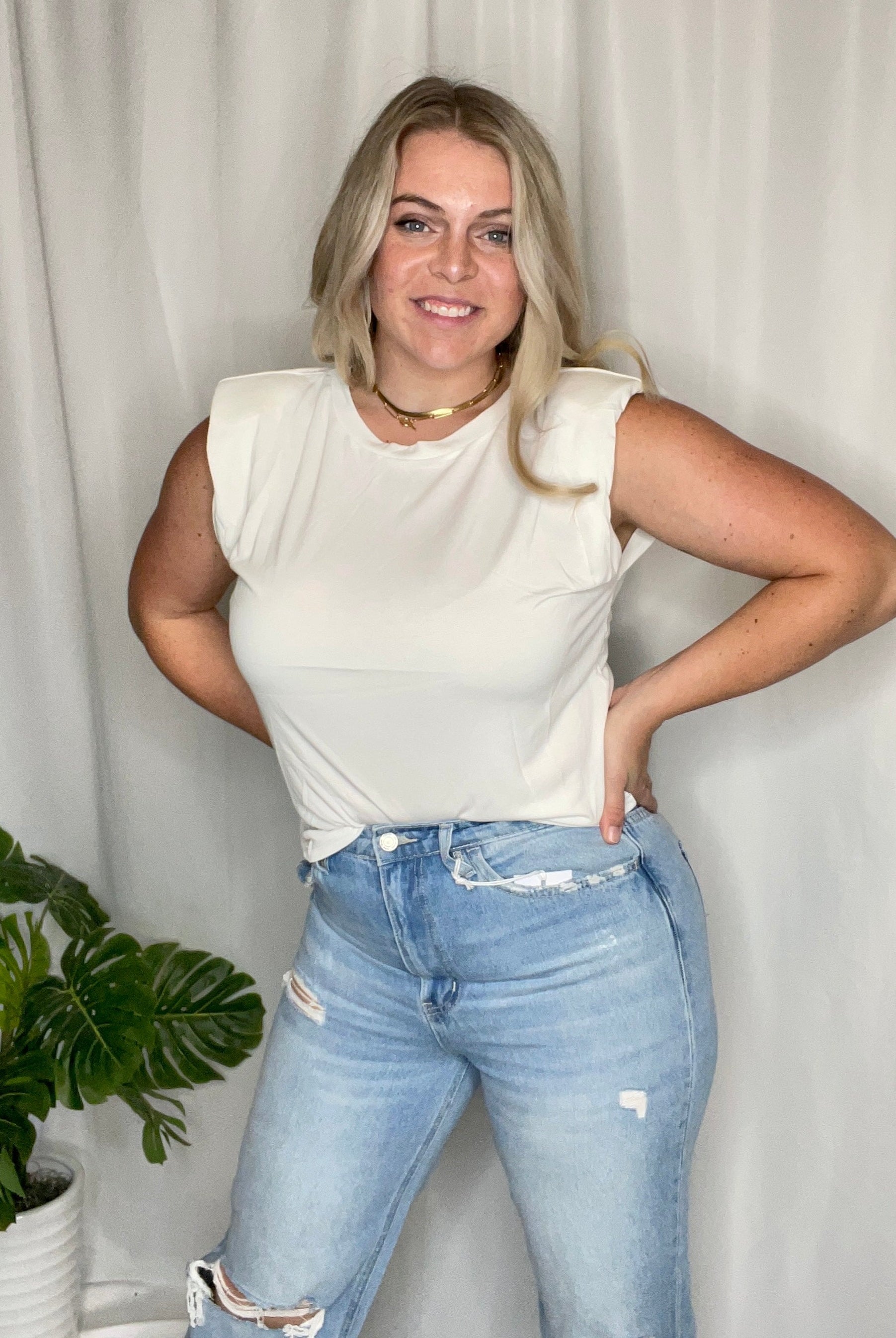 A woman wearing a white tank top with shoulder pads and a rounded neckline.