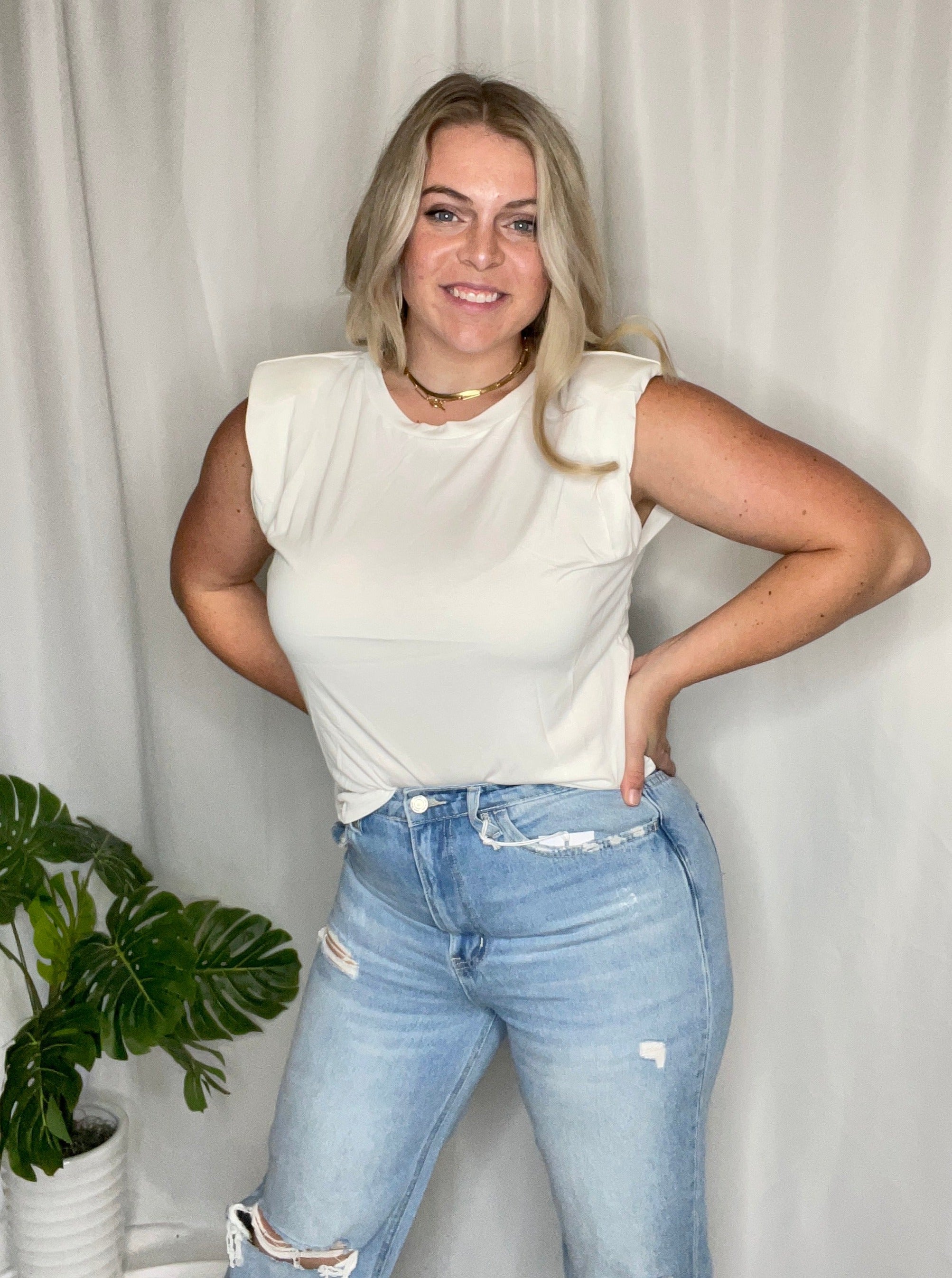 A woman wearing a white tank top with shoulder pads and a rounded neckline.